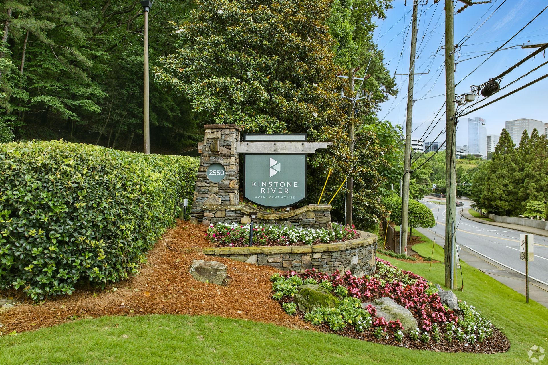 Stone entrance sign for a residential community with landscaping and a street in the background.