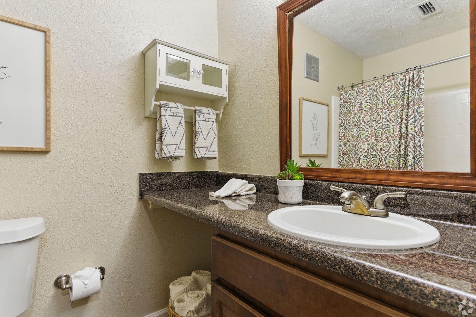 Bathroom with a brown countertop, white sink, and dark-framed mirror.  White cabinet above countertop, with towels hanging.