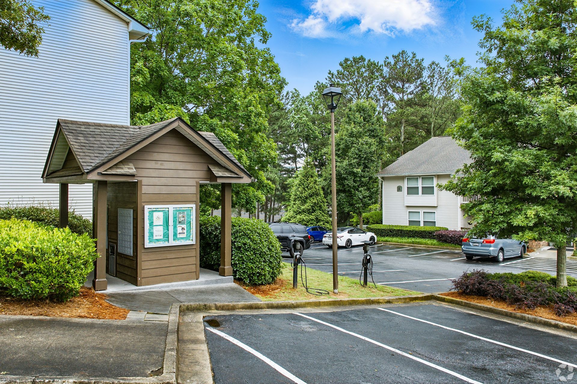 Brown information kiosk with green signs, parking lot, and apartment building in the background.