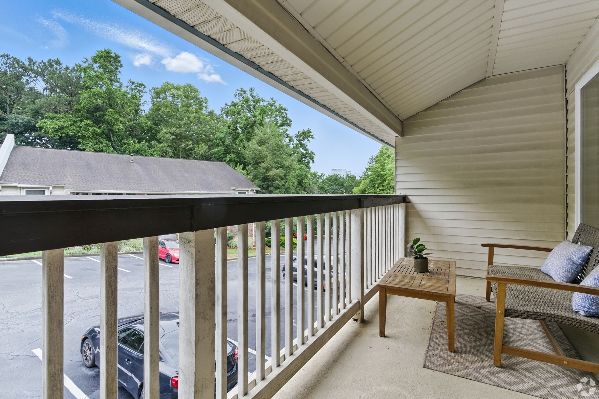 Balcony with seating, overlooking a parking lot and trees.