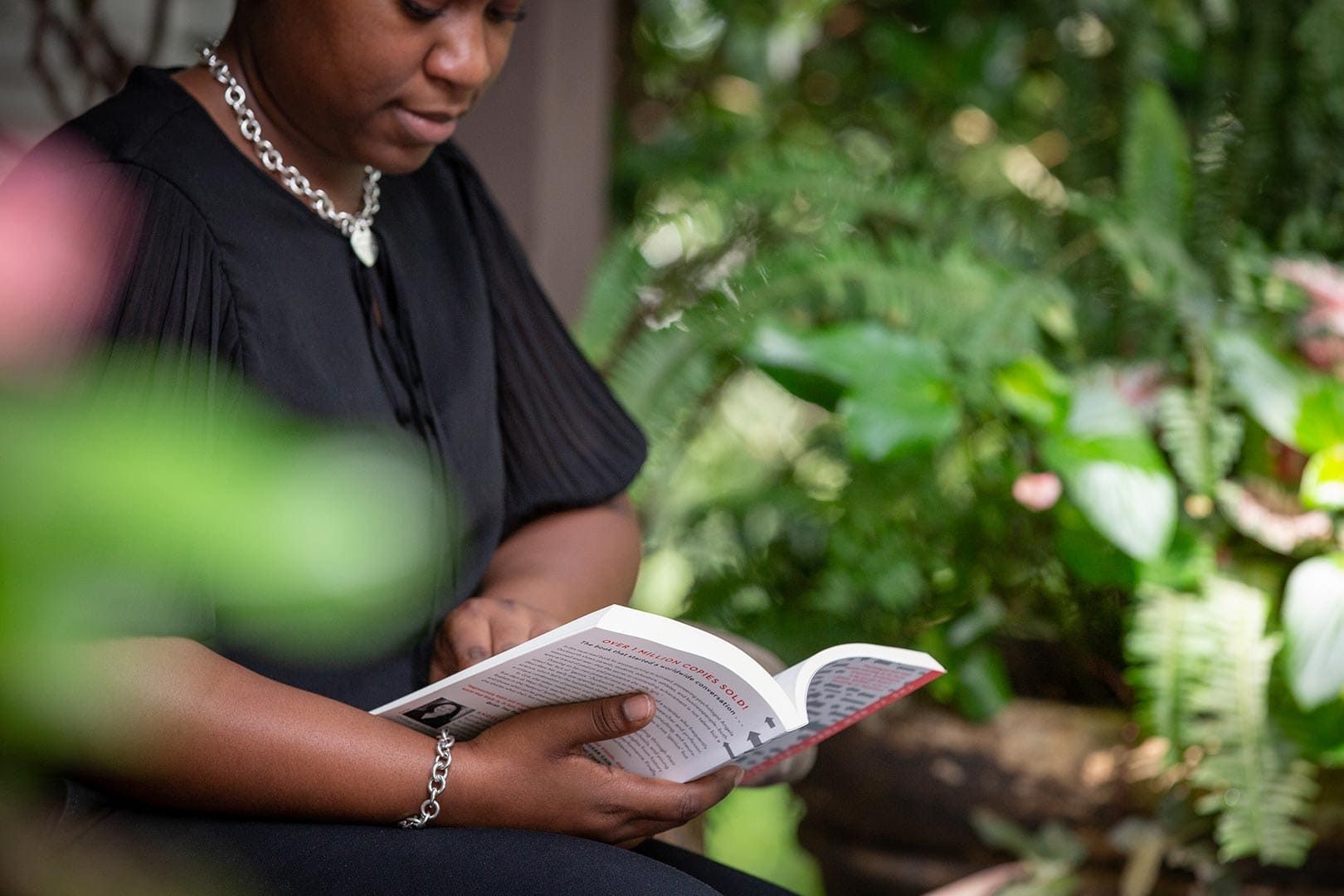 A woman is sitting on a bench reading a book.