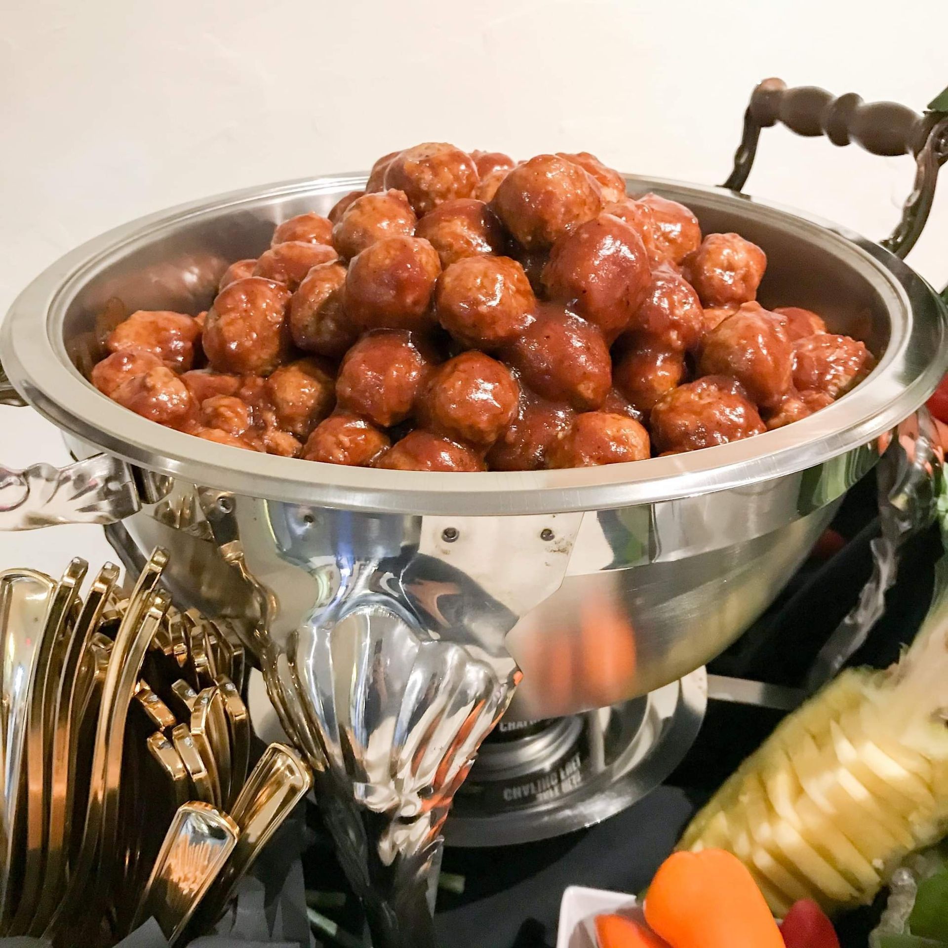 A silver bowl filled with meatballs and sauce on a table