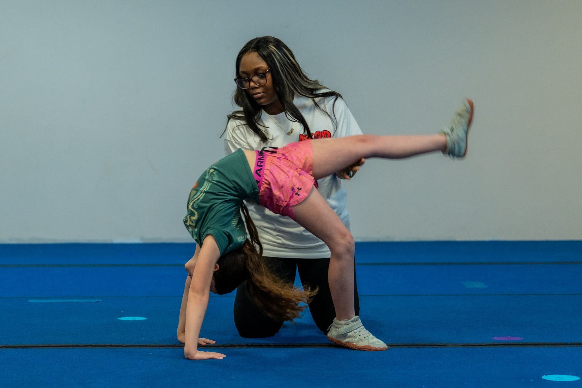 A gymnastics coach spotting a student practicing a backbend on a blue mat.