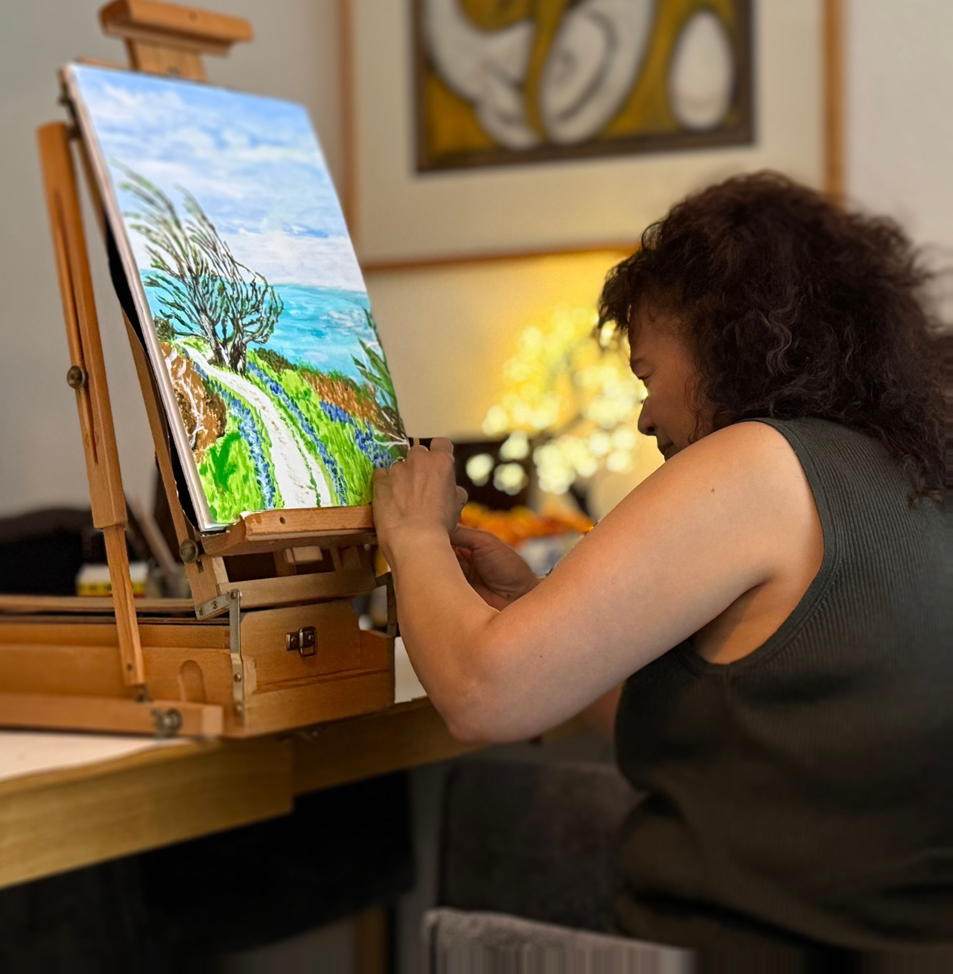 Een persoon schildert een kleurrijk landschap op een schildersezel in een gezellige binnenruimte.