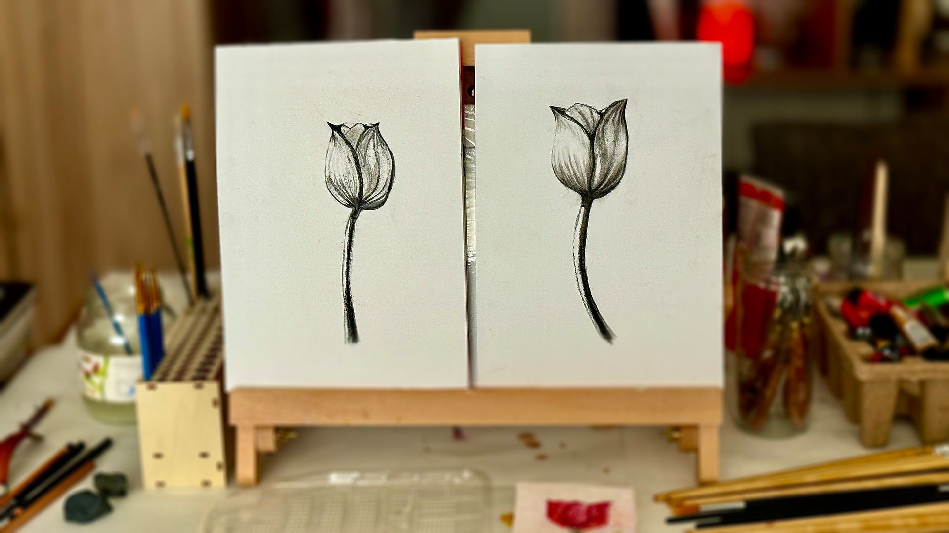 Twee kleine zwart-wit schetsen van tulpen op een houten schildersezel in een kunstenaarsatelier.