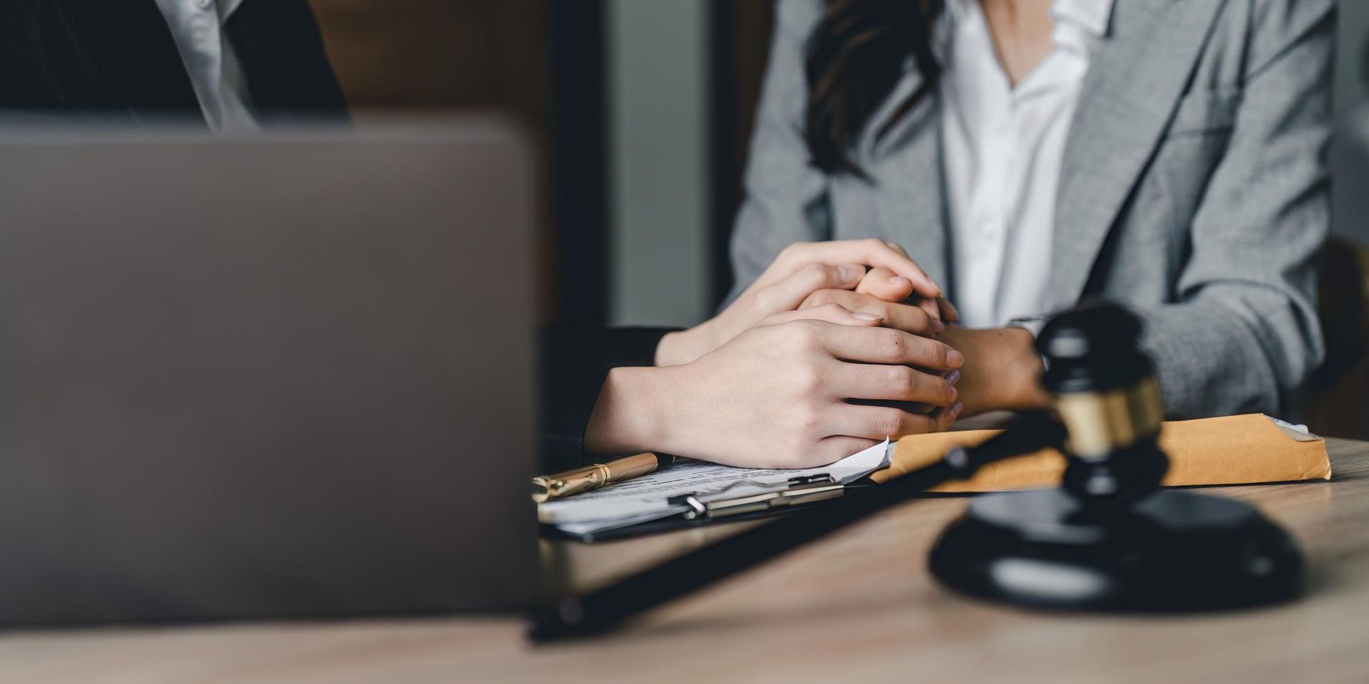 Attorney at desk with laptop and gavel, hands clasped in a law office