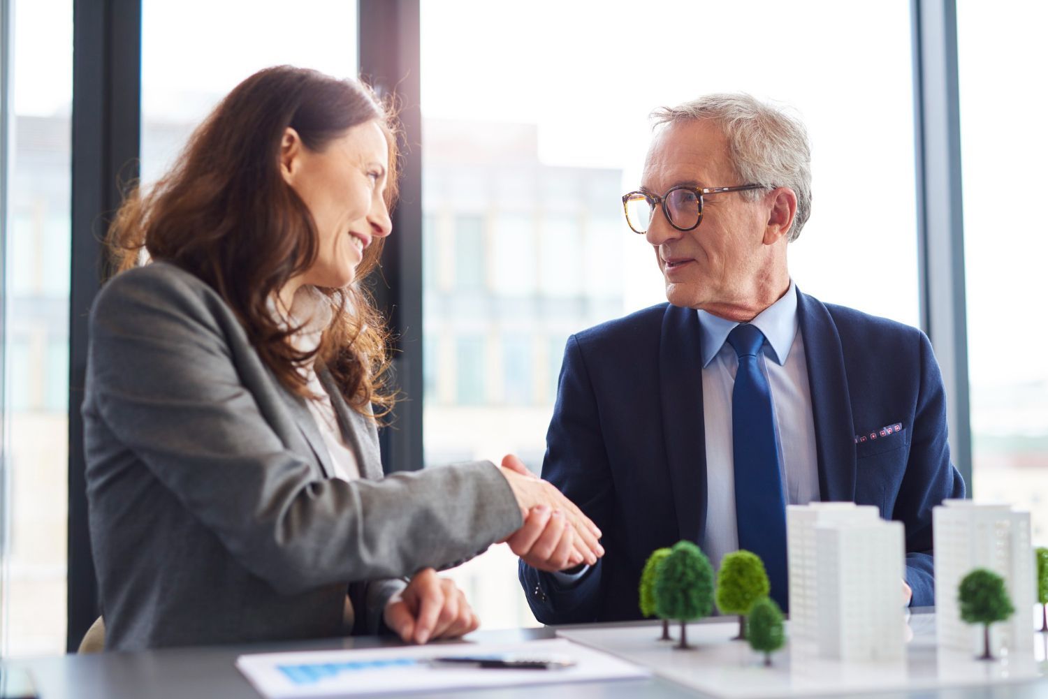 Two businesspeople discussing a project over a table with building models in a bright office