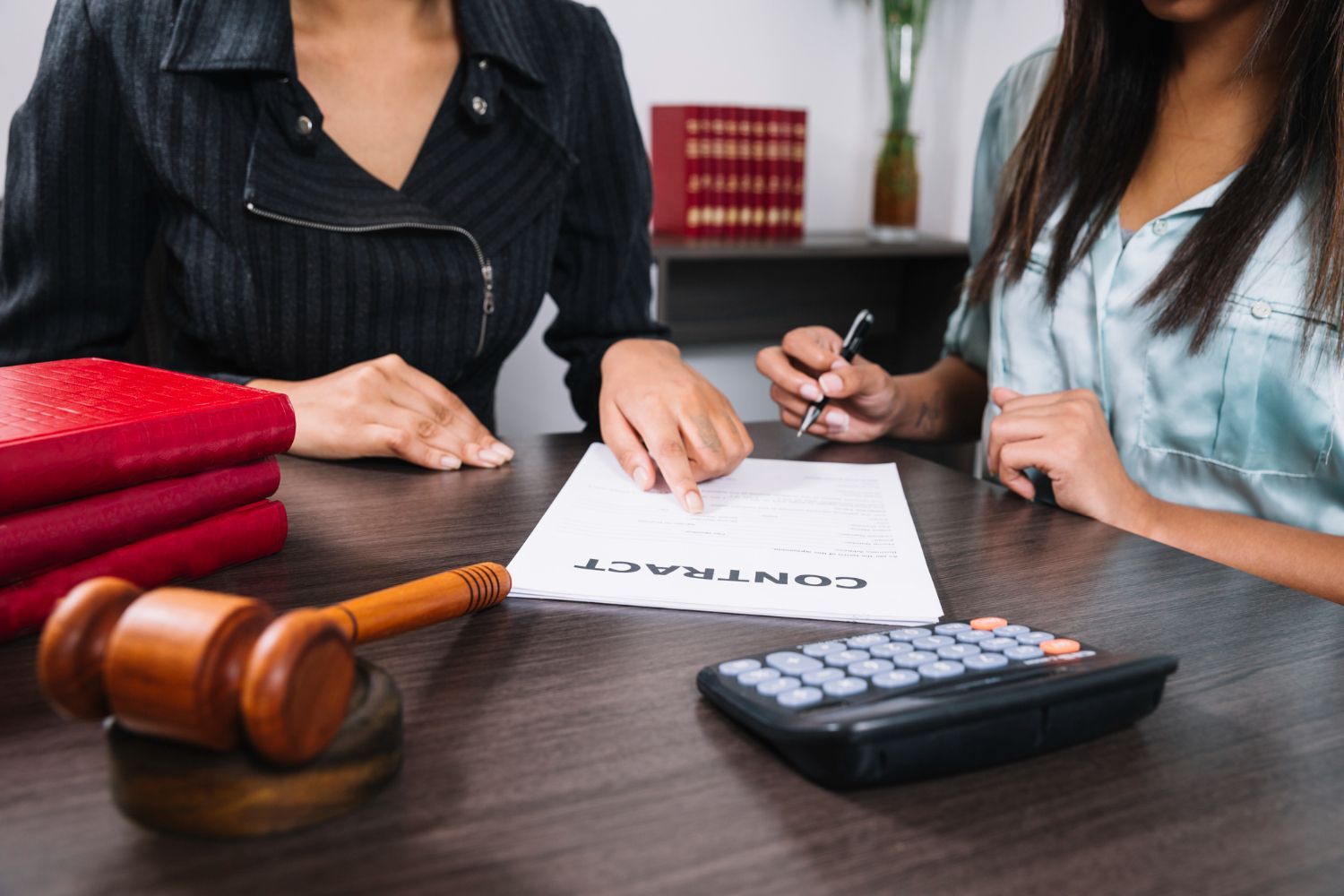 Lawyer reviewing a contract with a client; gavel, calculator, and red file folders on the desk