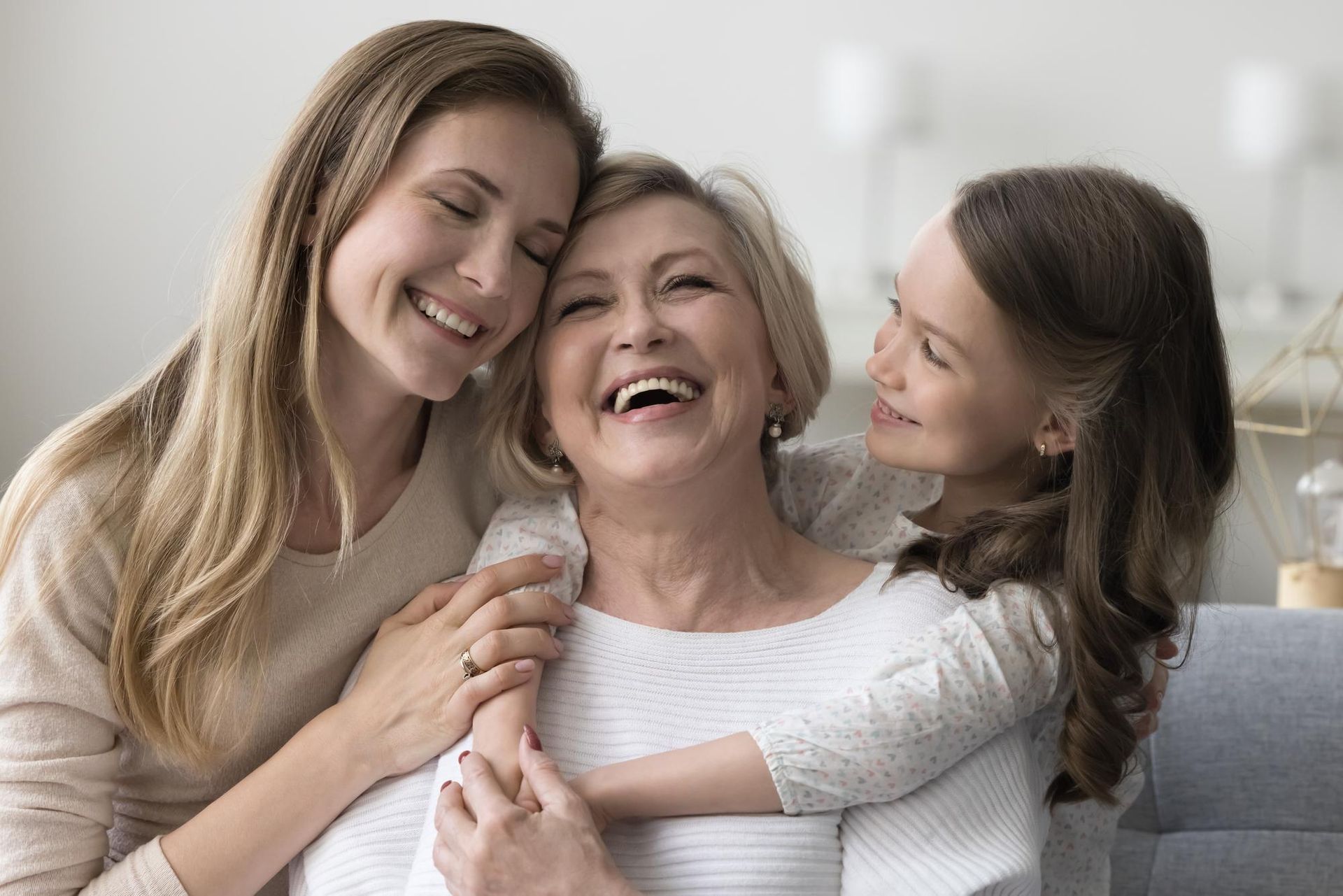 Three smiling people embracing on a couch in a bright, cozy room