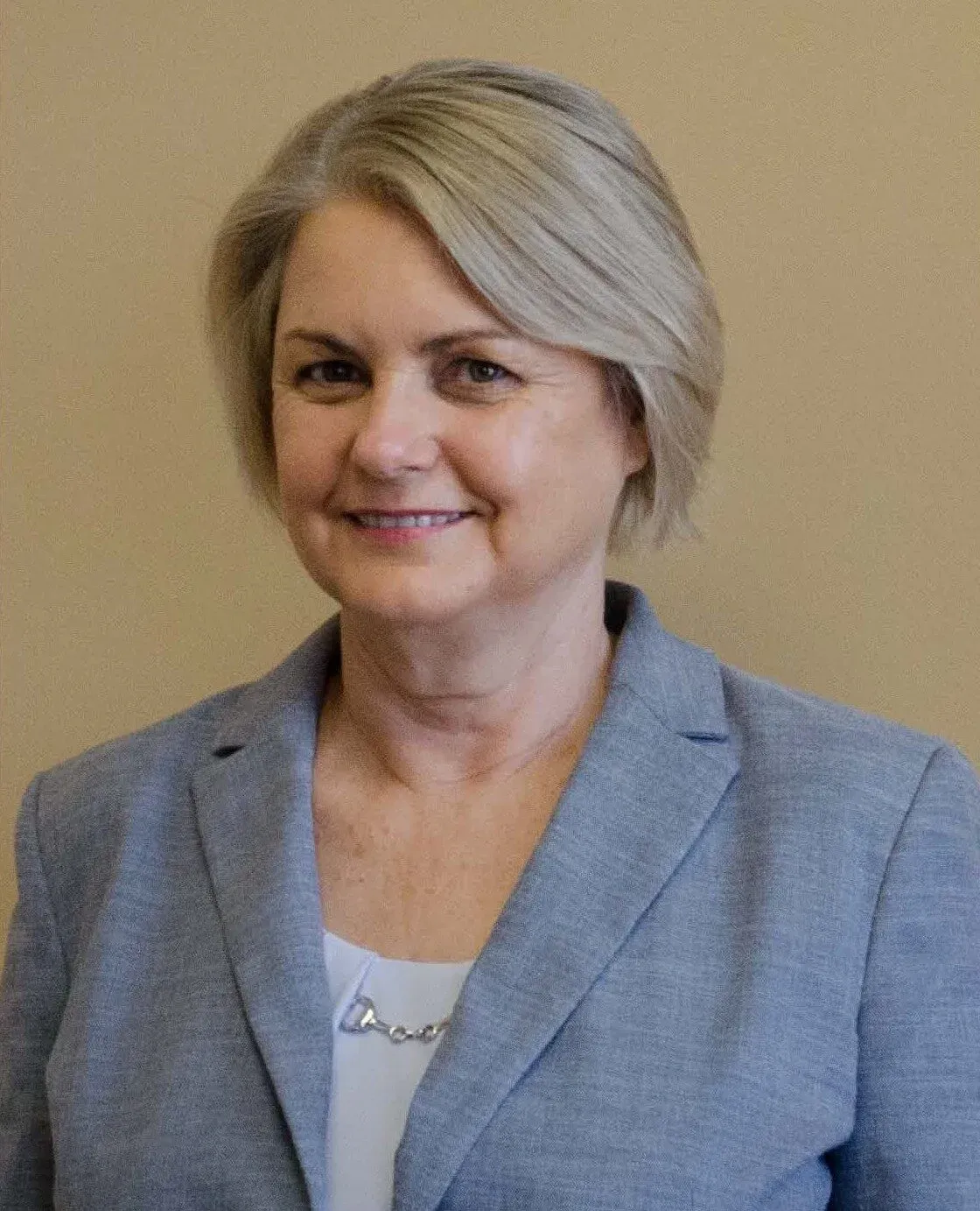 Portrait of a smiling person in a light blue blazer against a beige background