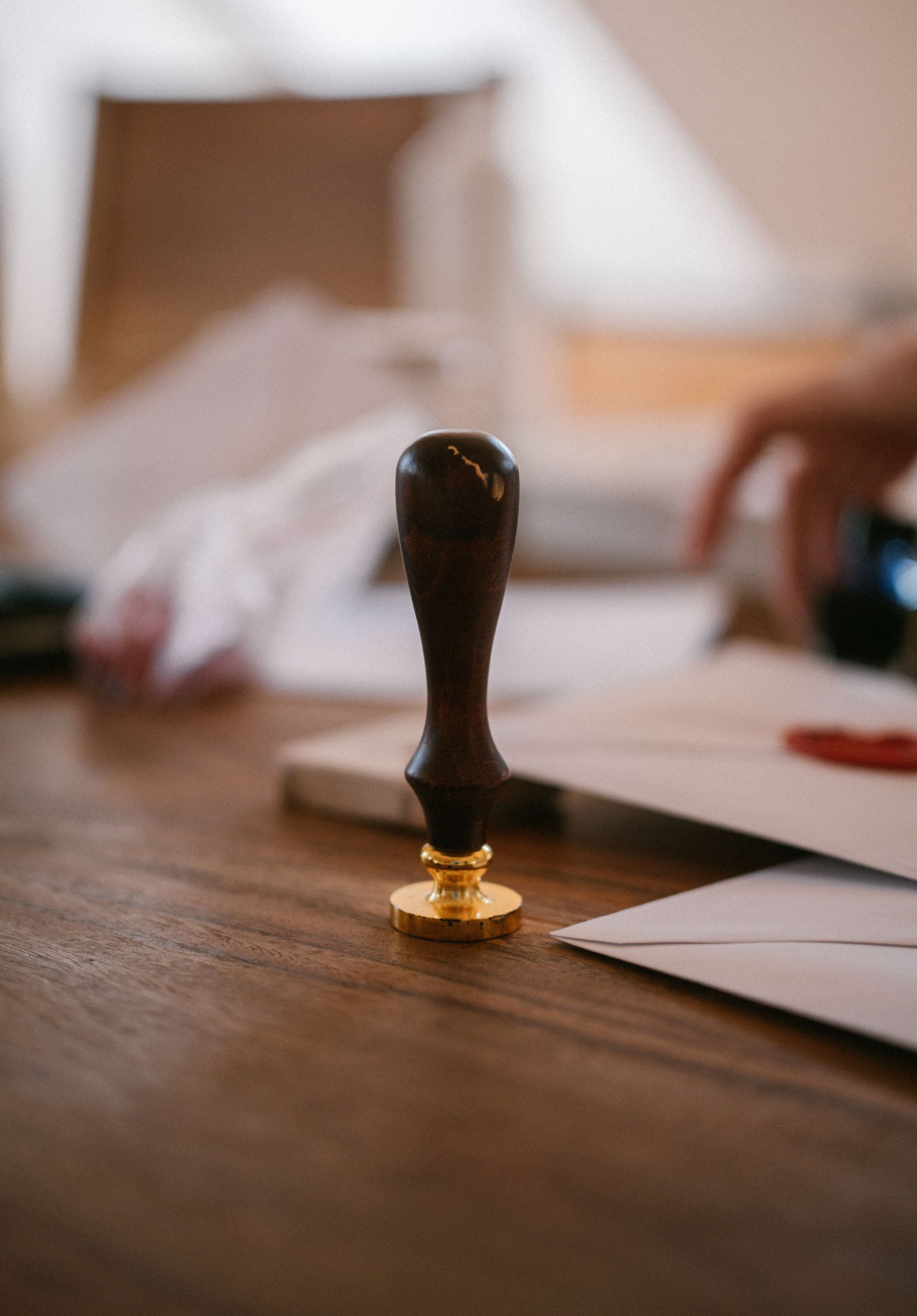 Black wax seal stamp on a wooden table with envelopes and blurred hands in the background