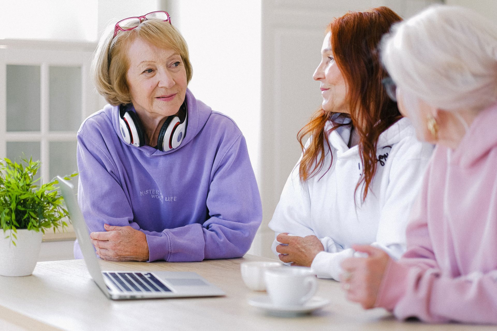 Three people talking at a table with a laptop and coffee in a bright office setting