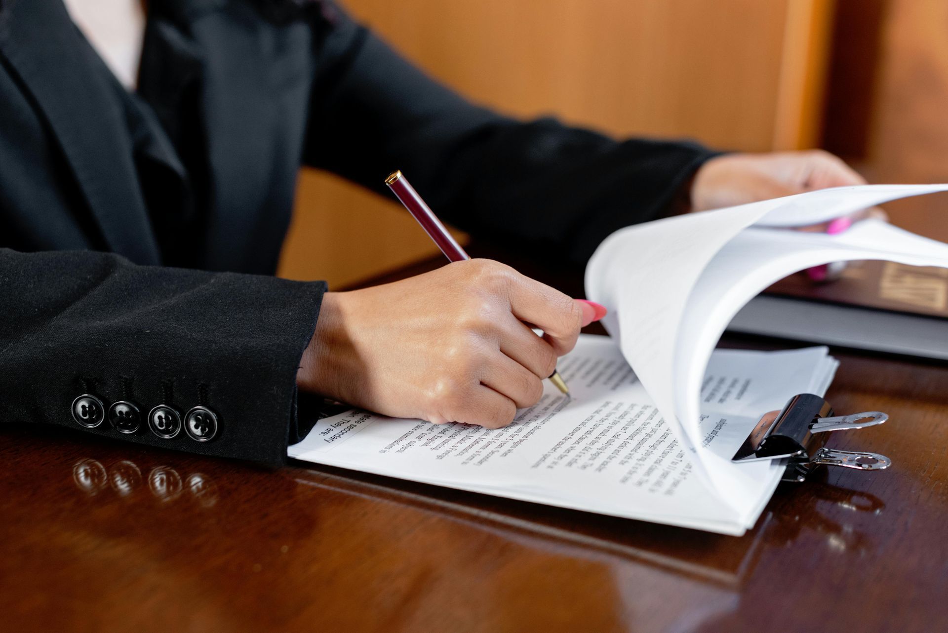 Person in a black suit writing with a pencil in an open book on a wooden desk.