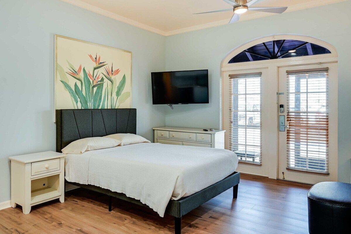 Bright bedroom with a bed, nightstand, wall art, TV, and French doors to a balcony