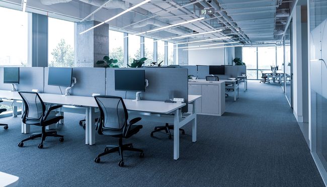 Empty modern office with desks, chairs, computers, and large windows. Blue and white color scheme.