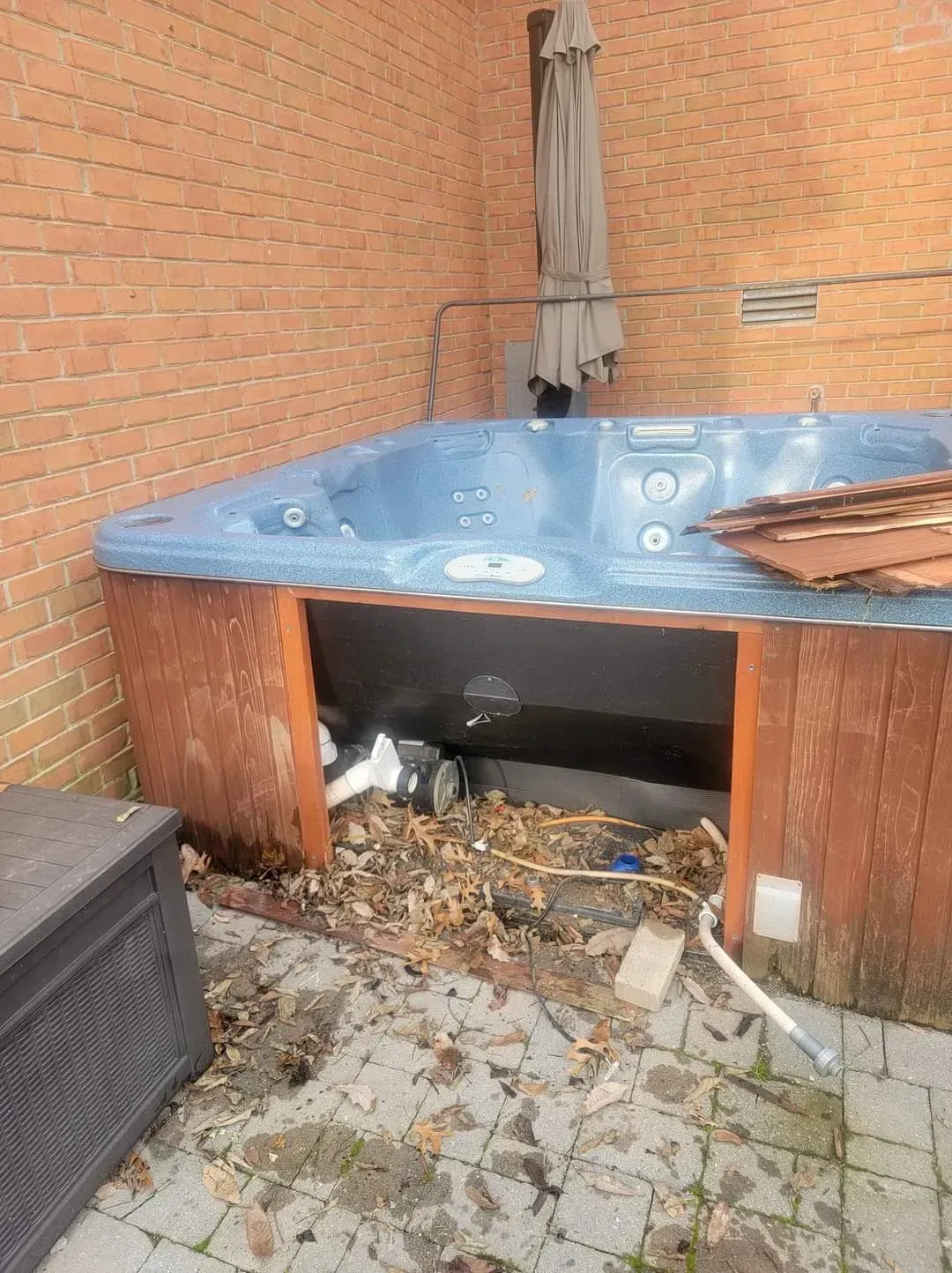 A blue hot tub is sitting on a brick patio next to a brick wall.
