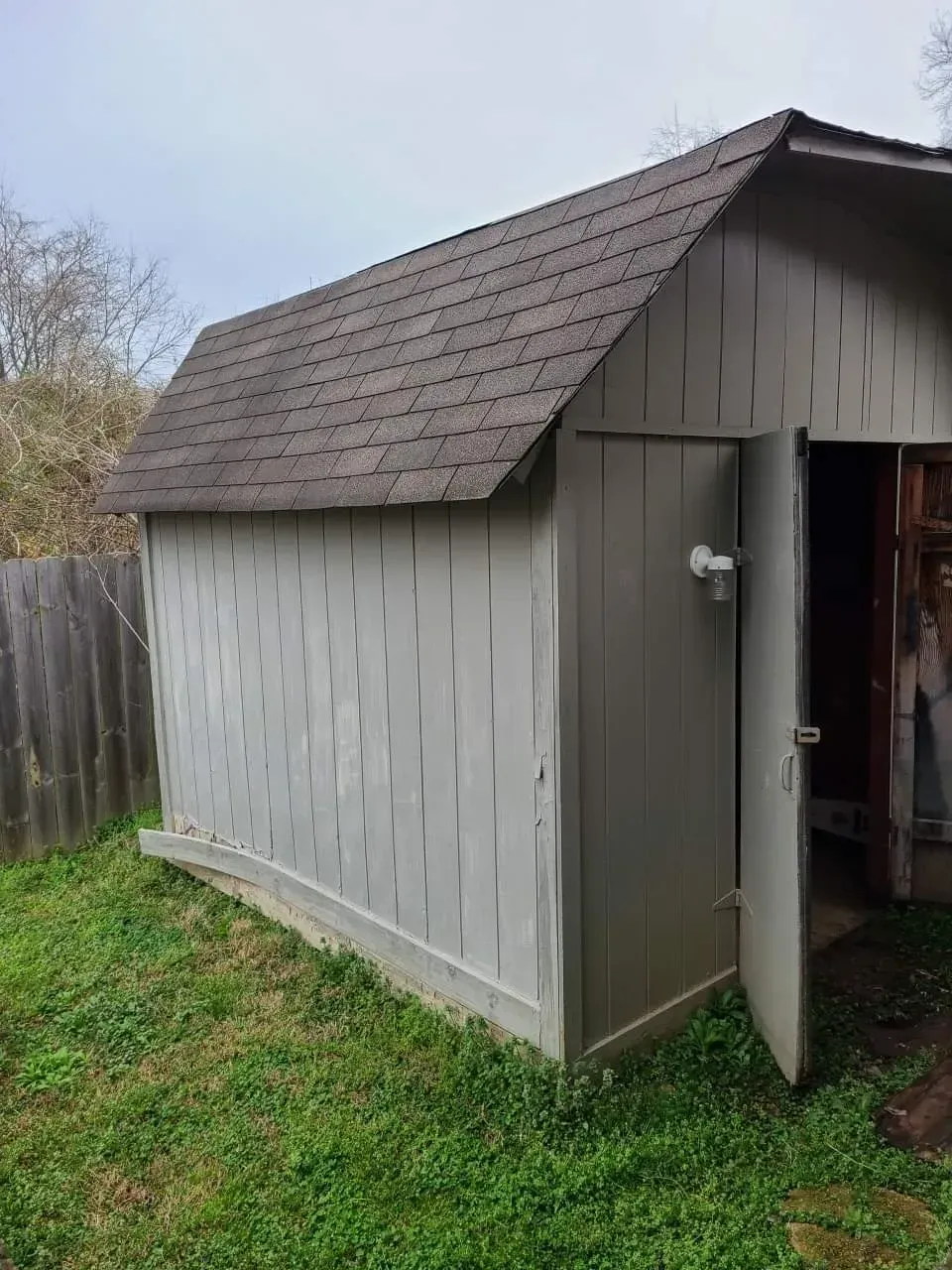 A shed with a roof and a door is sitting in the grass.