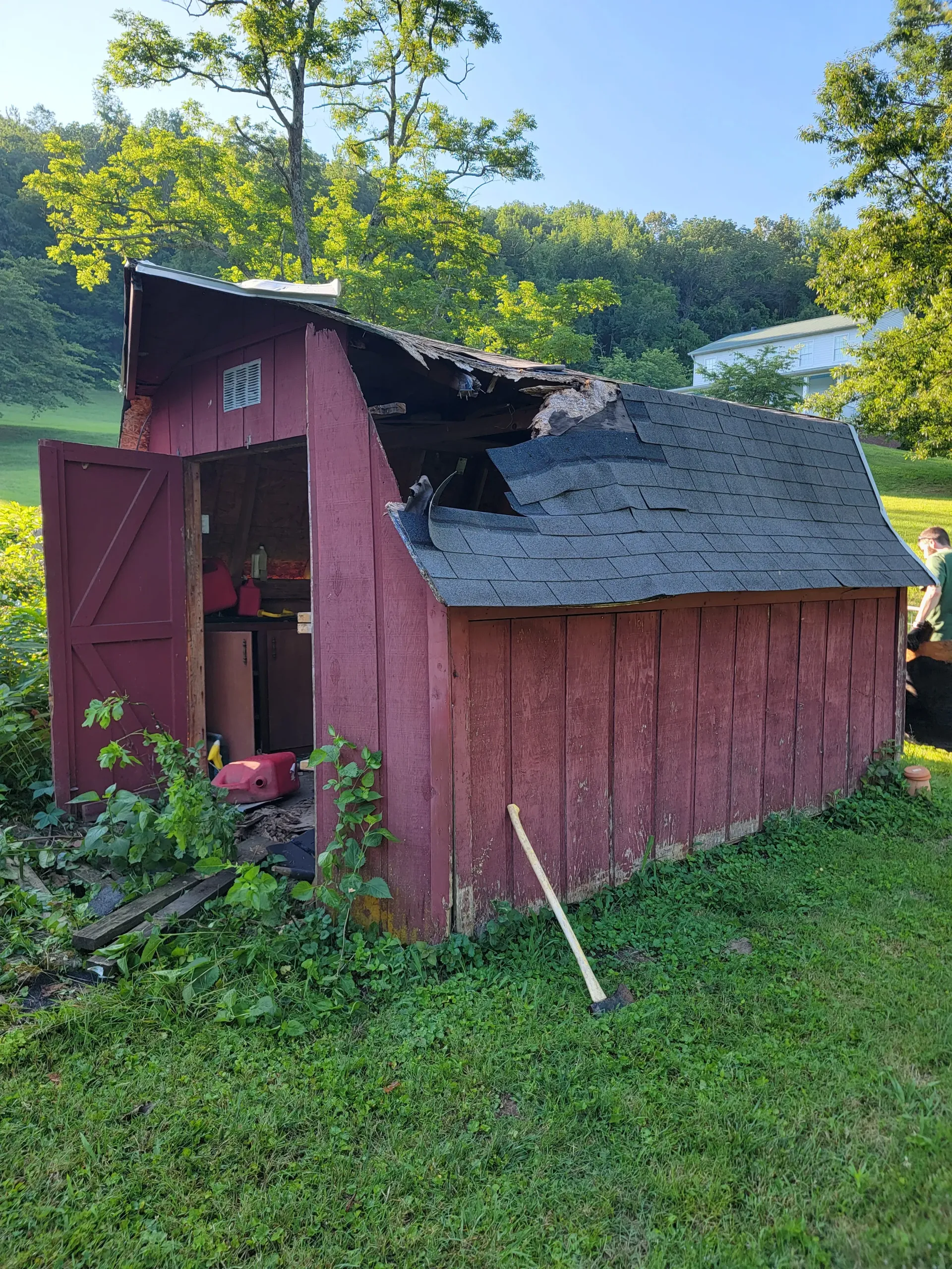 A red barn with a roof that has been damaged by a fire.