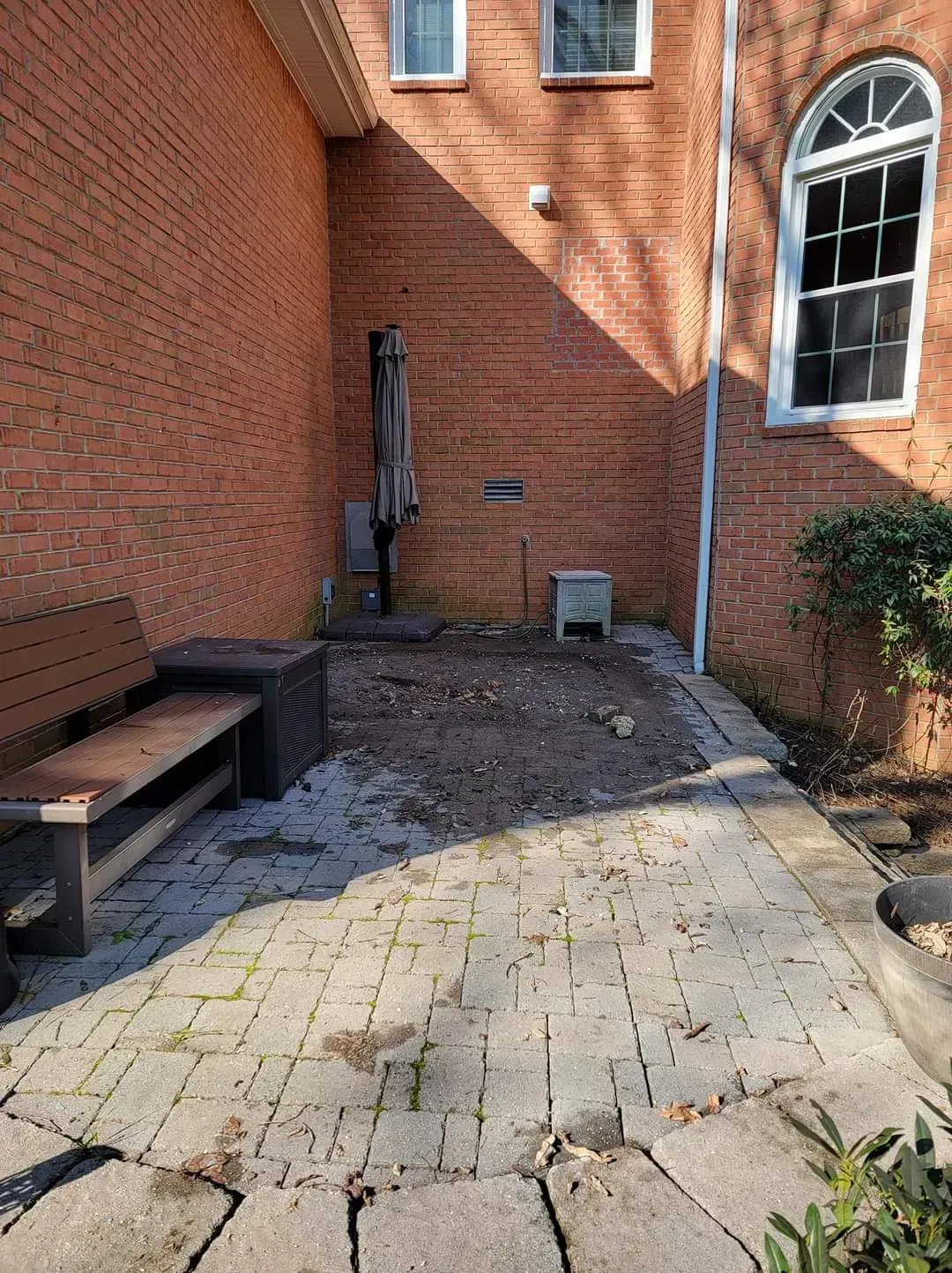 There is a bench and umbrella in the backyard of a brick house.