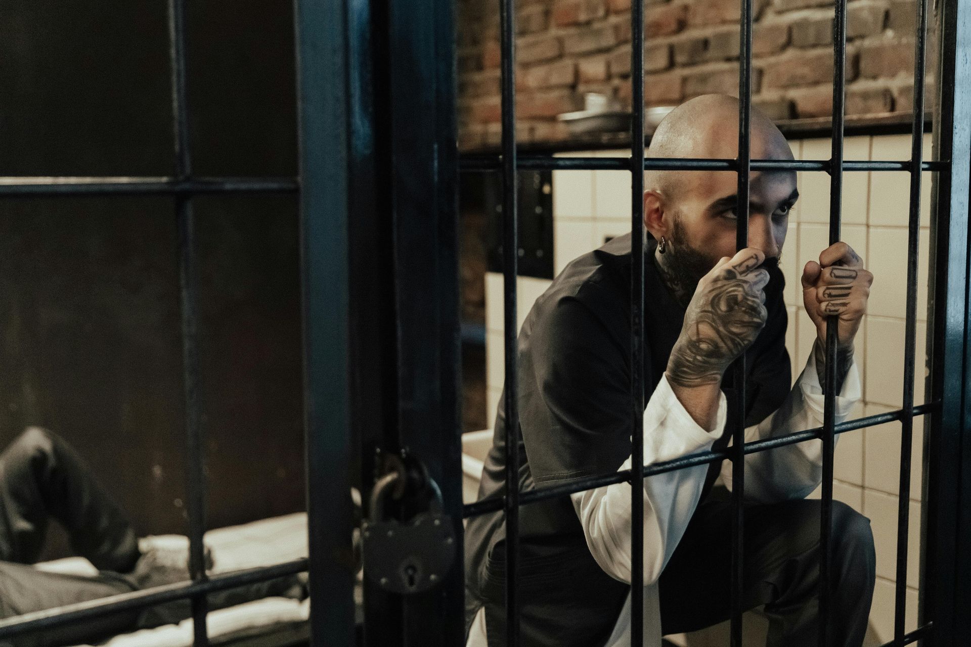 Man crouching behind bars in a dim prison cell, gripping the bars and looking out