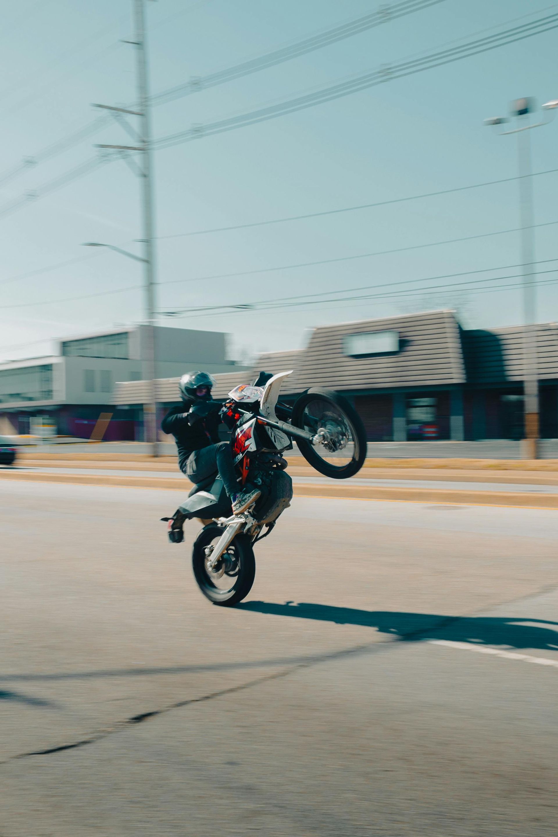 Motorcyclist doing a wheelie on a city street with buildings and power lines in the background