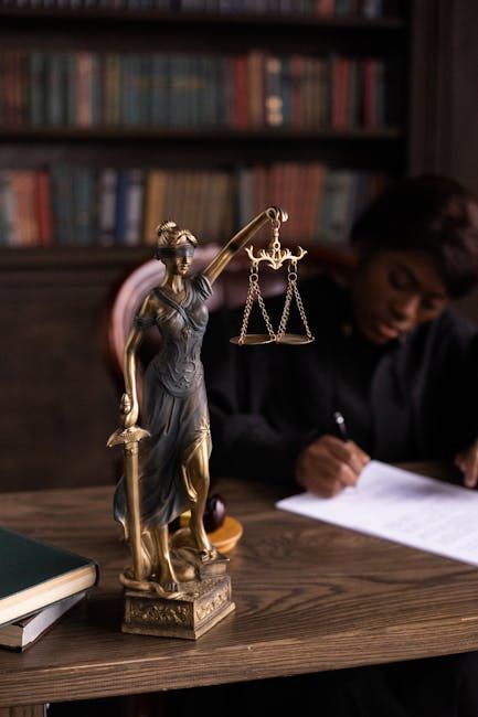 Bronze Lady Justice statue on desk with person writing in blurred law office background