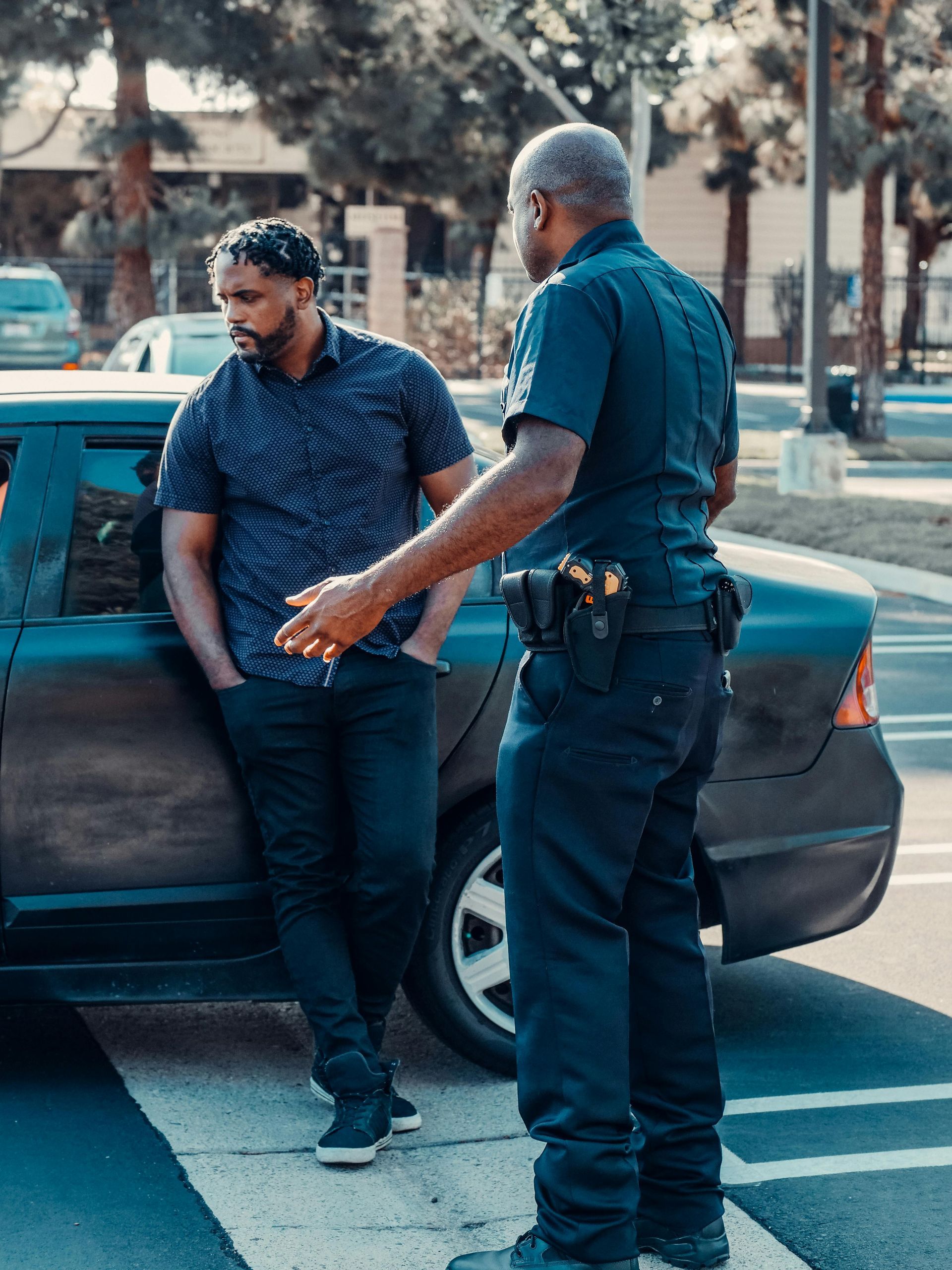 Police officer speaking with a man leaning against a car on a city street
