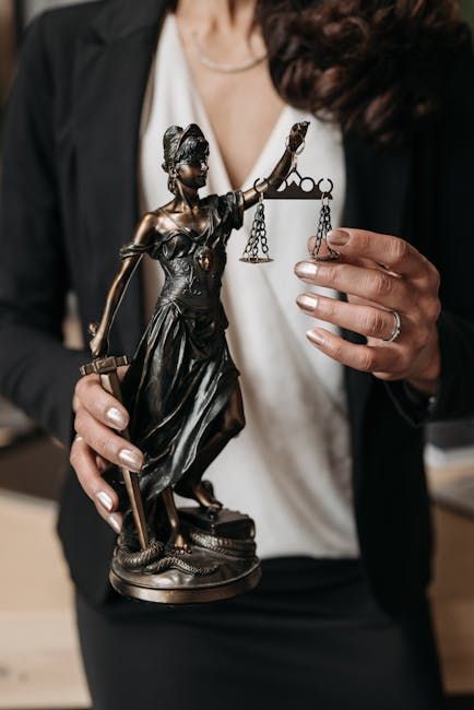 Person holding a small bronze Lady Justice statue with scales and sword; blurred indoor background