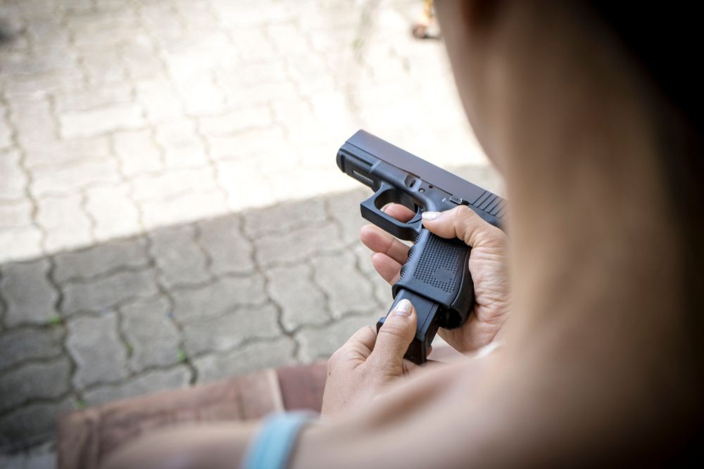 Close-up of hands loading a black handgun outdoors on a paved surface