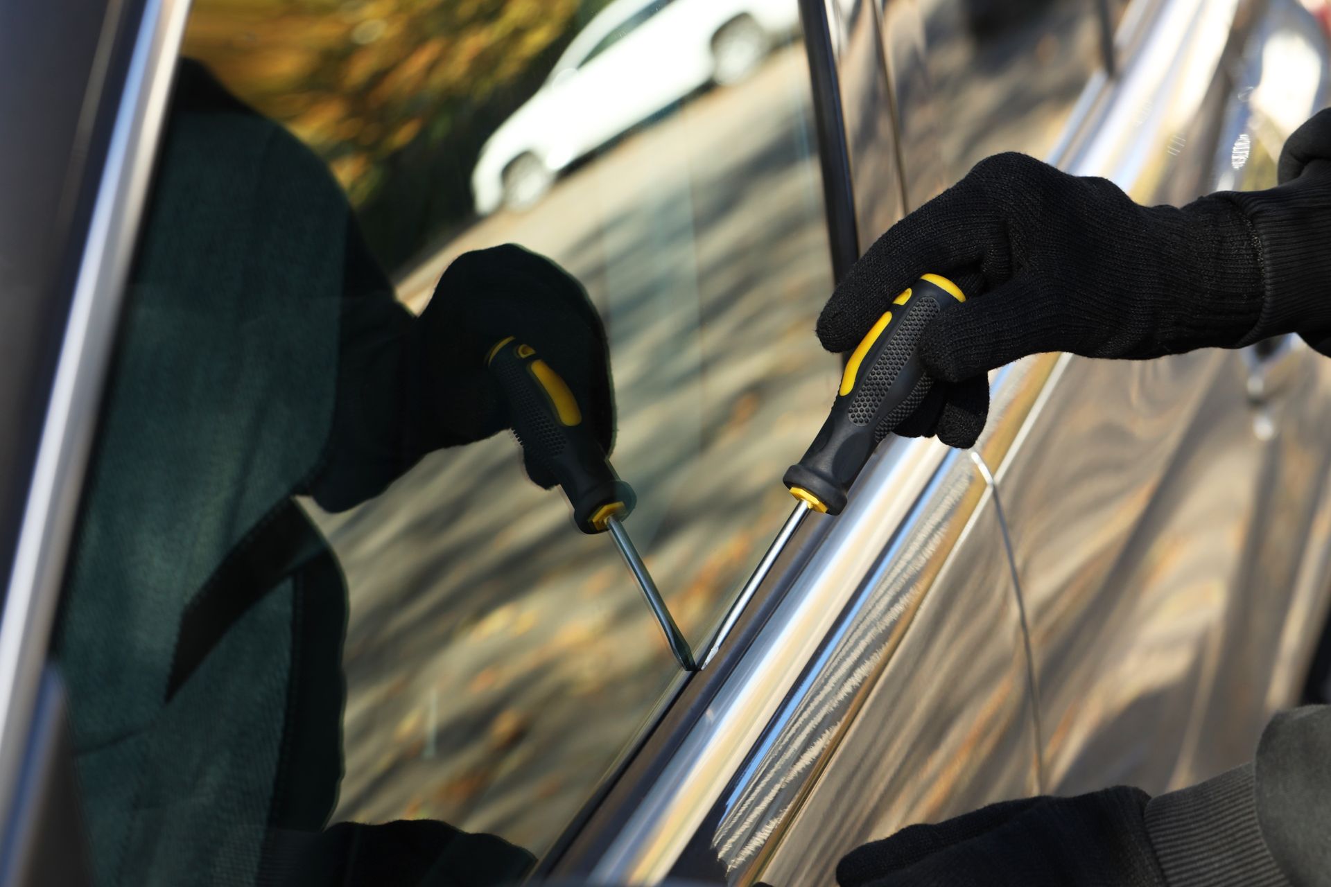 Black-gloved hands clean a car window with a squeegee and cloth.