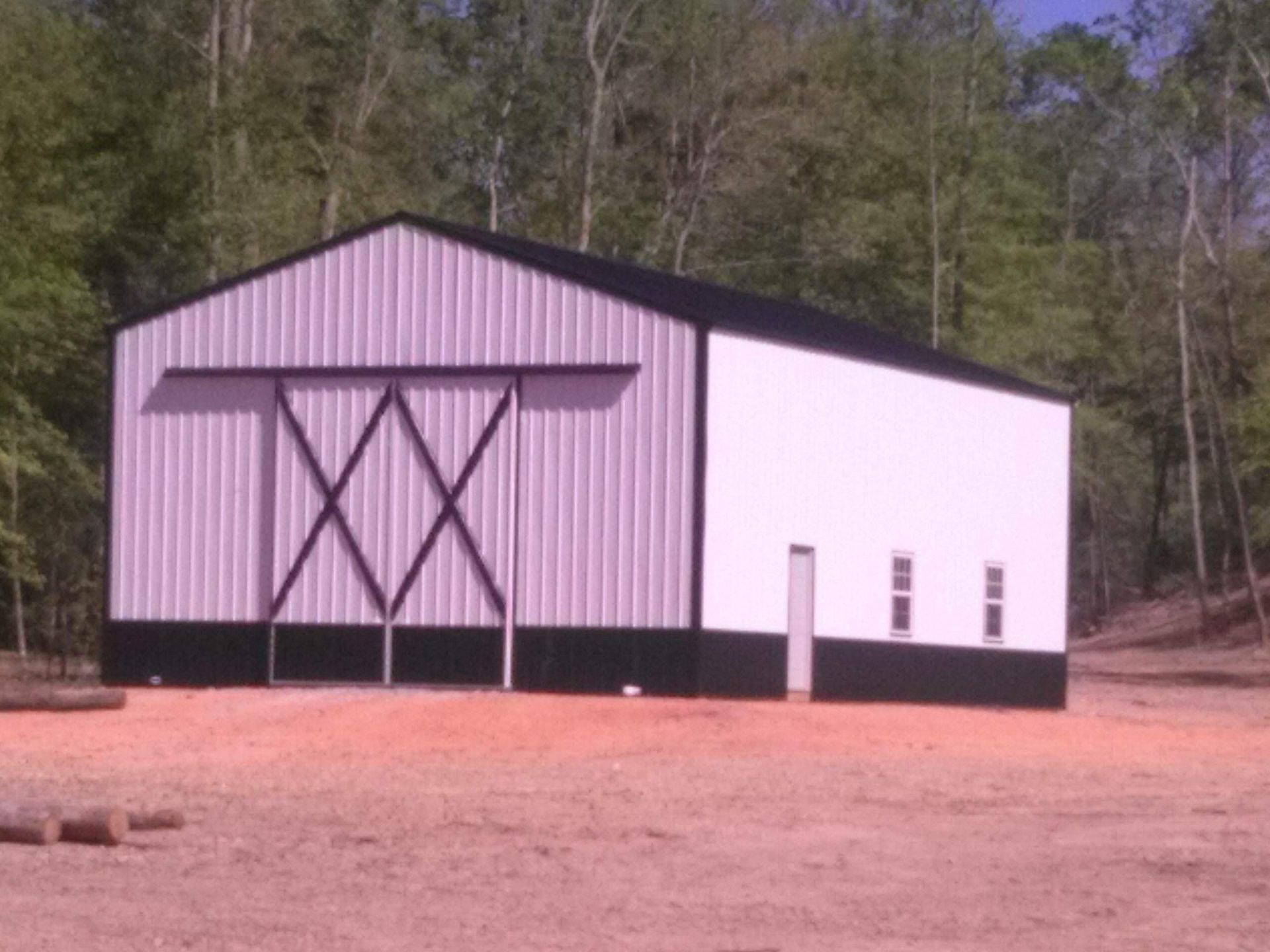 A white and black barn with a sliding door is sitting in the middle of a dirt field.