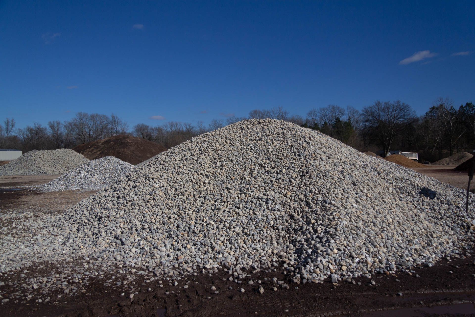 A pile of gravel in a field with trees in the background