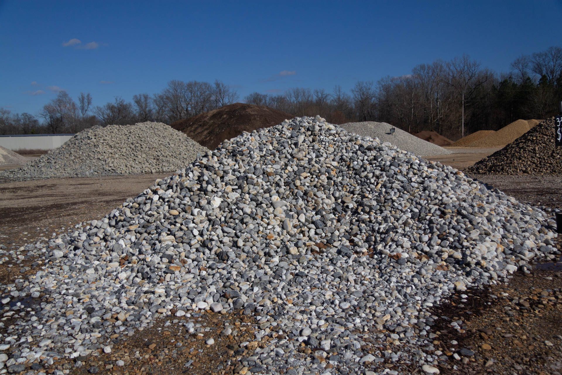 A pile of gravel in a field with trees in the background