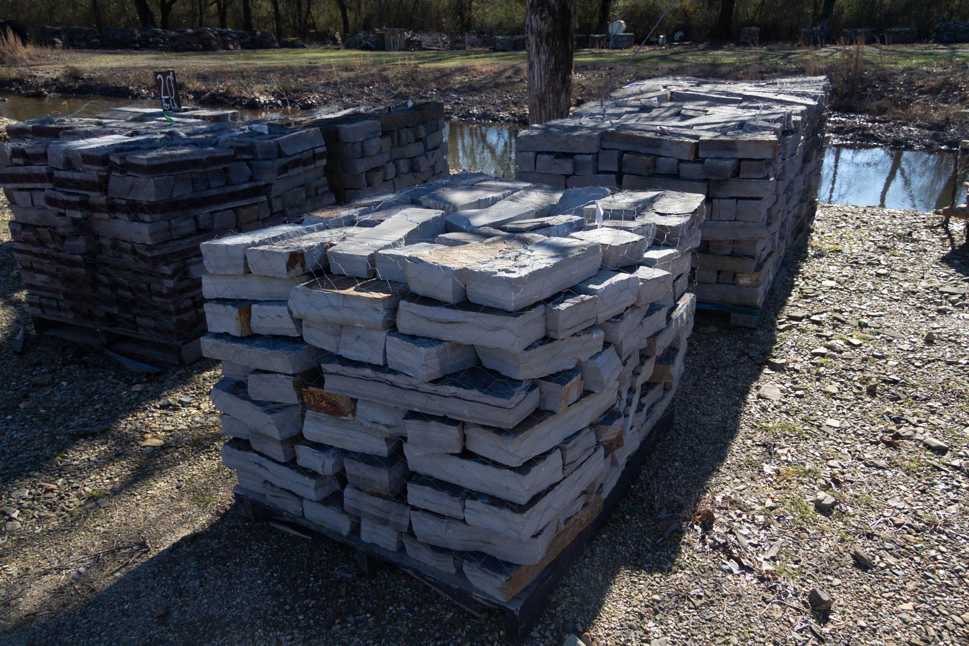 A pile of bricks is sitting in the dirt near a body of water