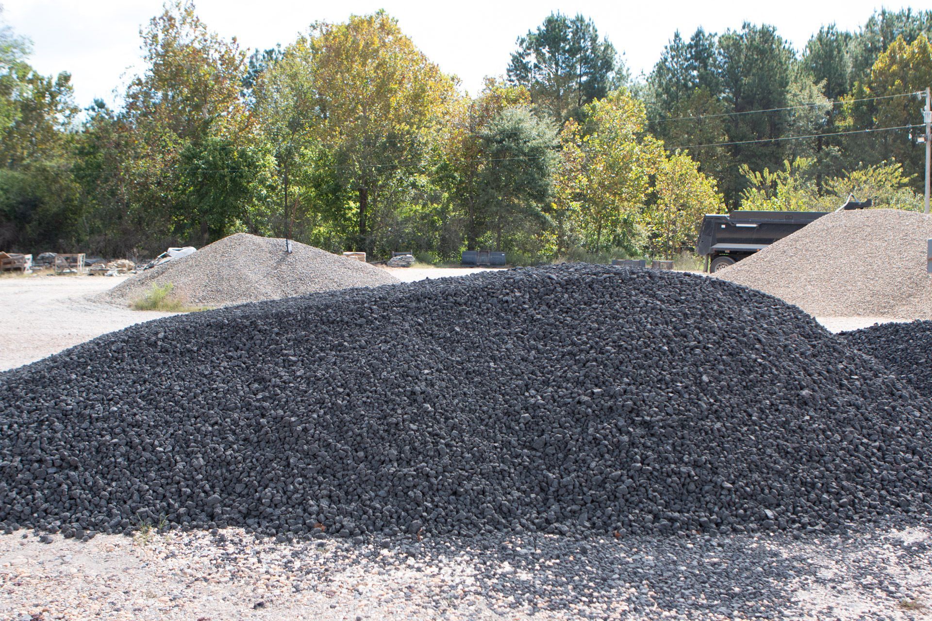 A pile of gravel is sitting in a field with trees in the background