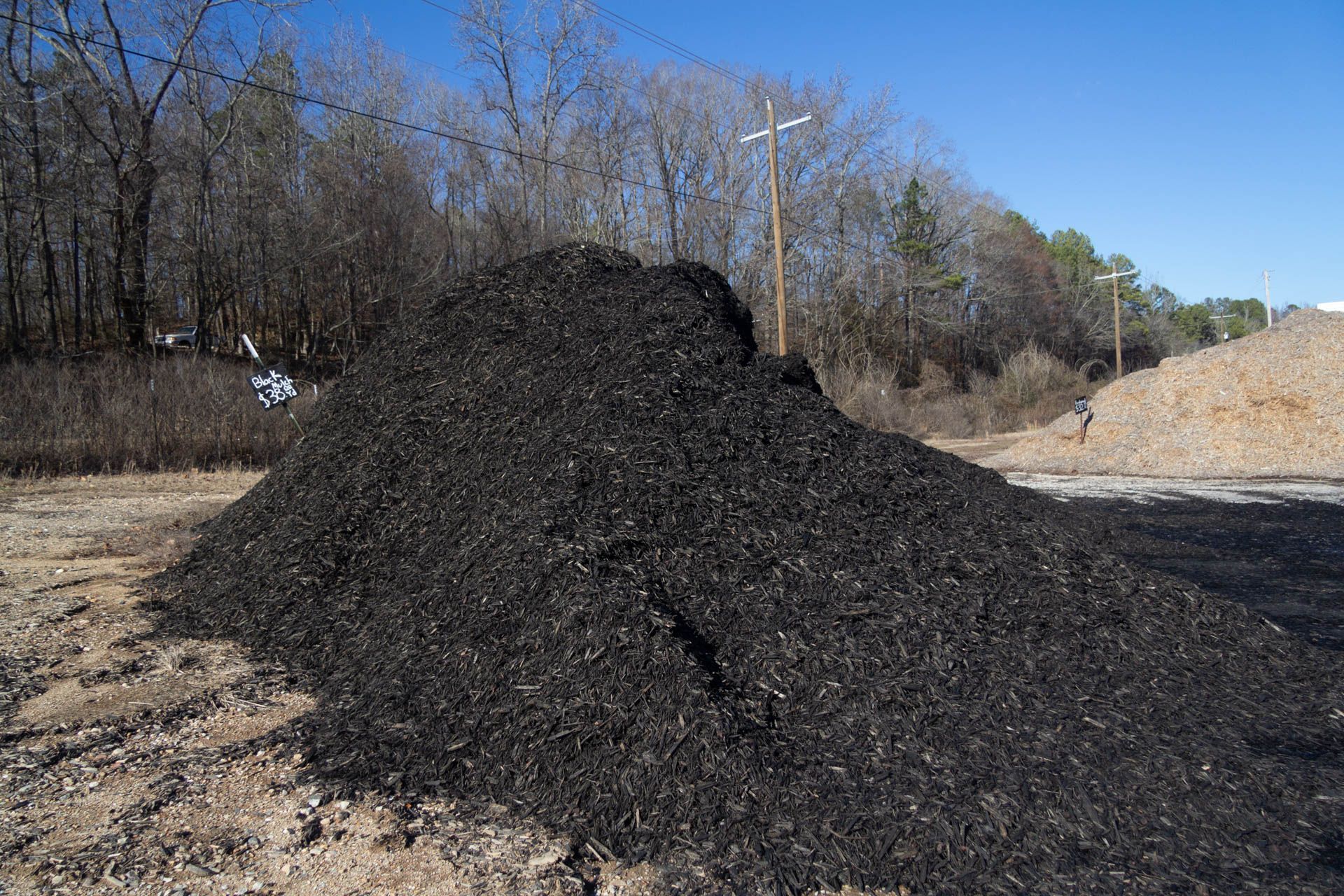 A large pile of black mulch is sitting on top of a dirt field.