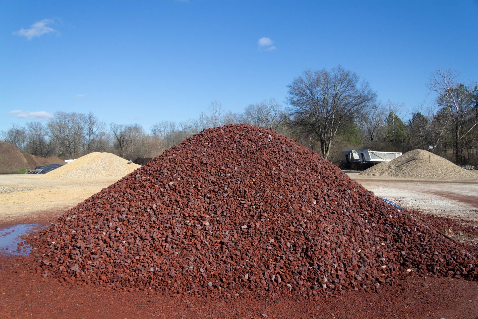 A pile of red gravel is sitting on top of a dirt field.