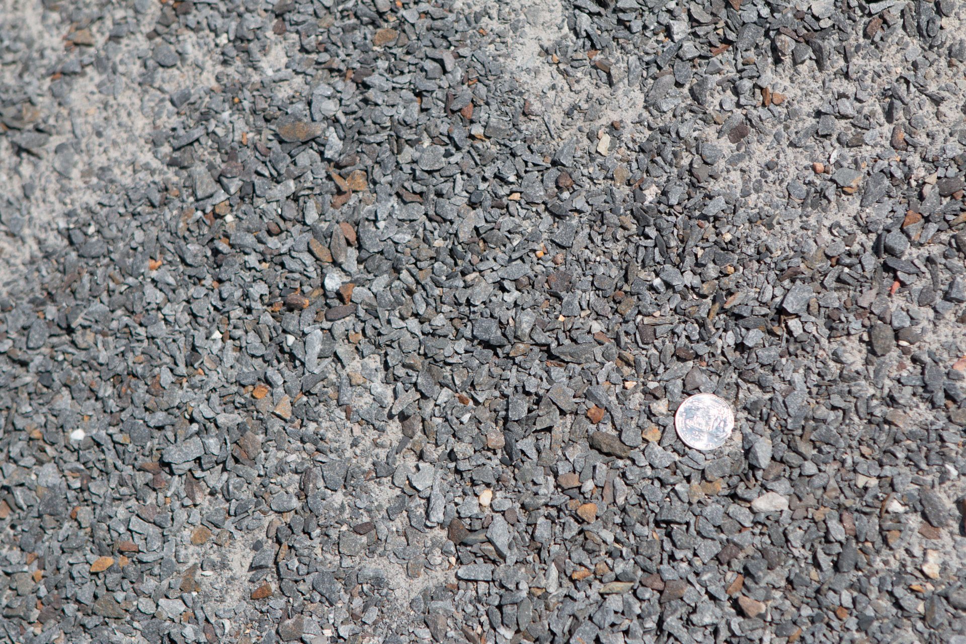A pile of gravel with a quarter in the middle.