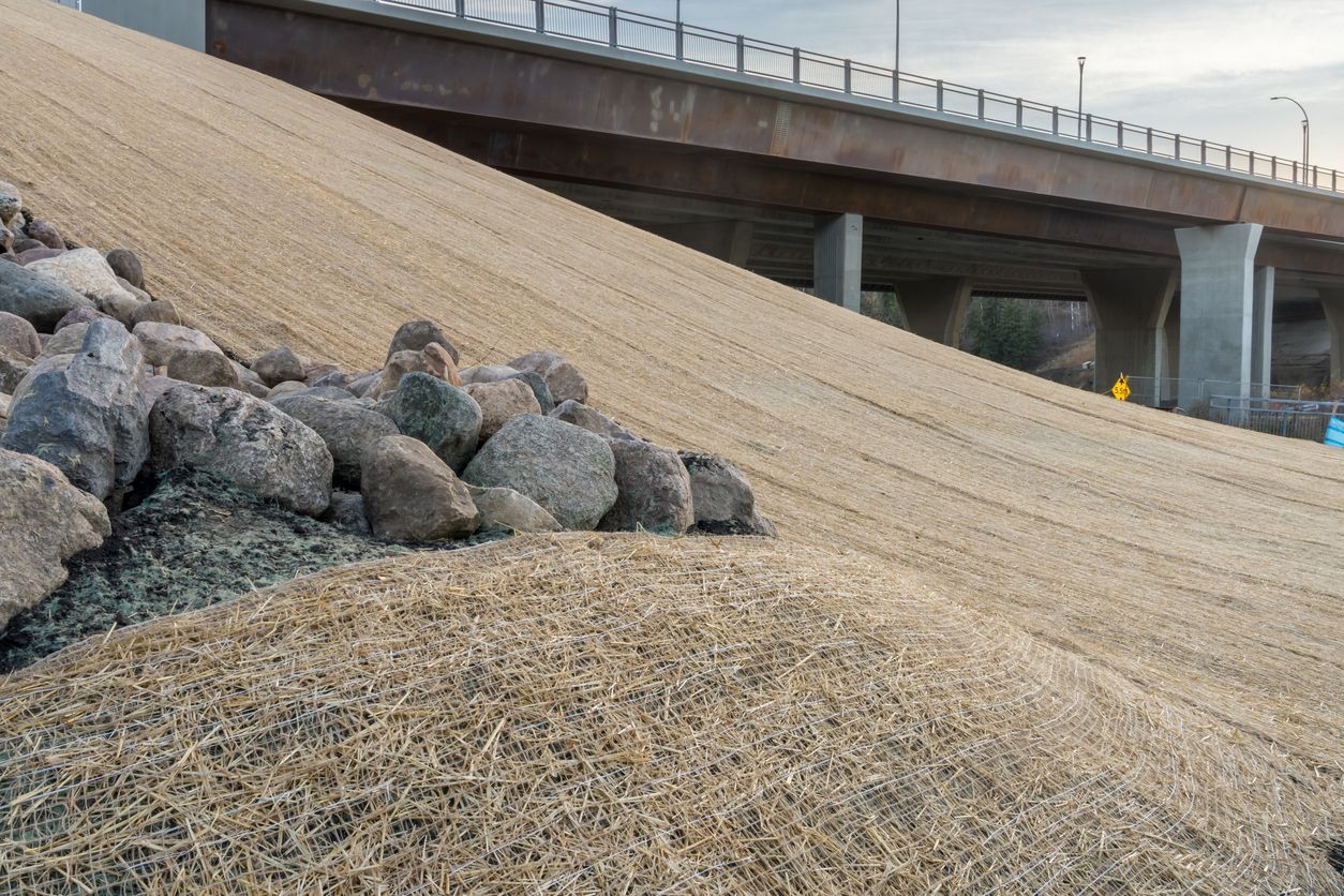 Rocks on a sloped embankment beside a bridge with dry grass or straw in the foreground