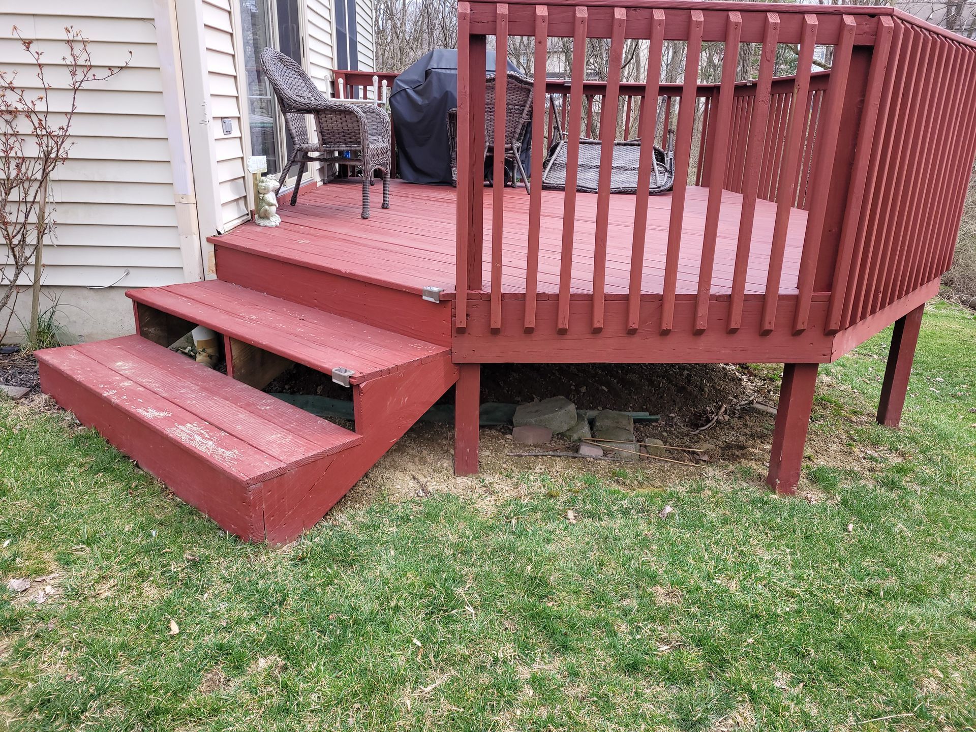 A red deck with stairs leading up to it is in the backyard of a house.