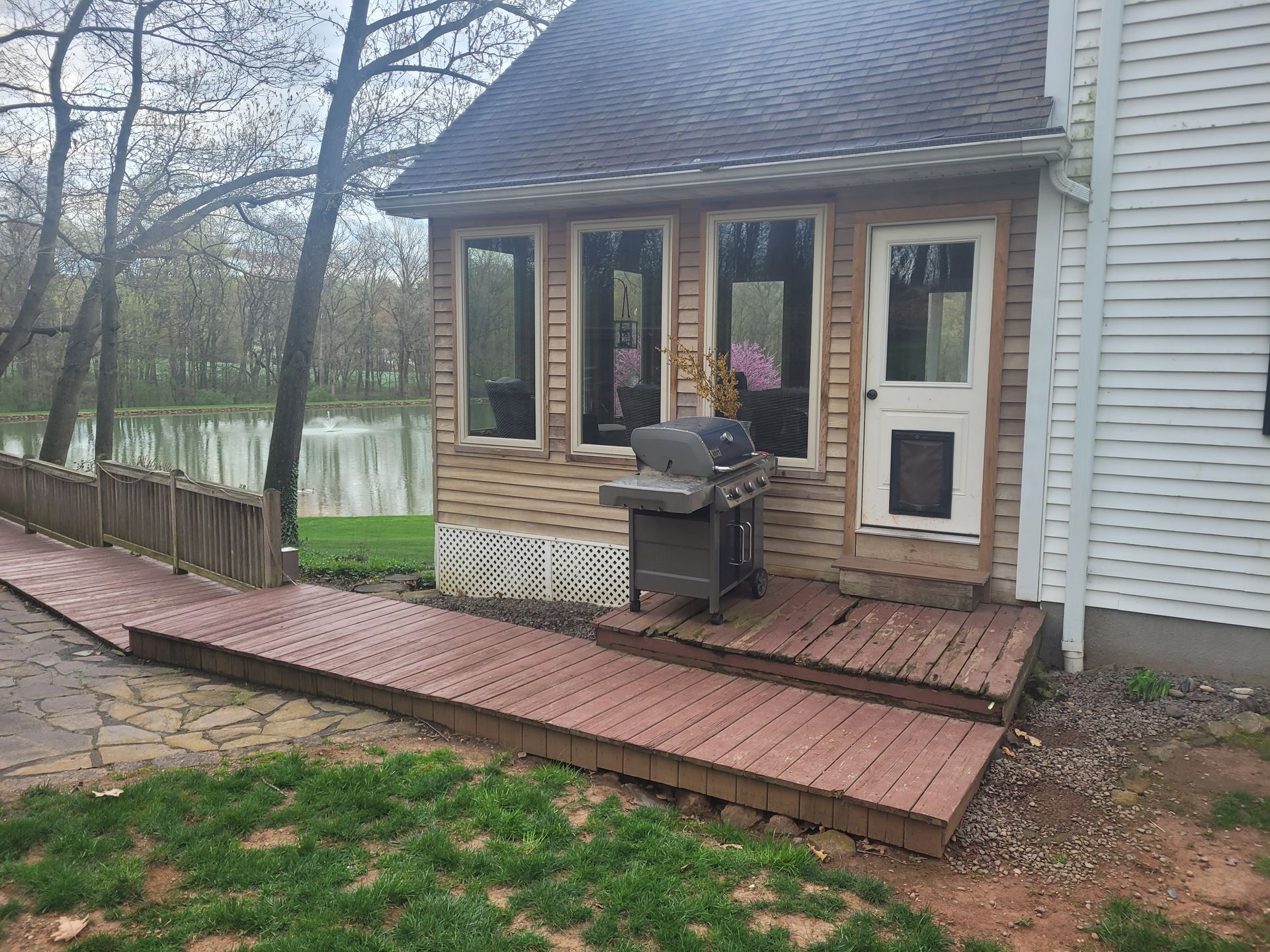 A house with a grill on the deck and a walkway leading to it.