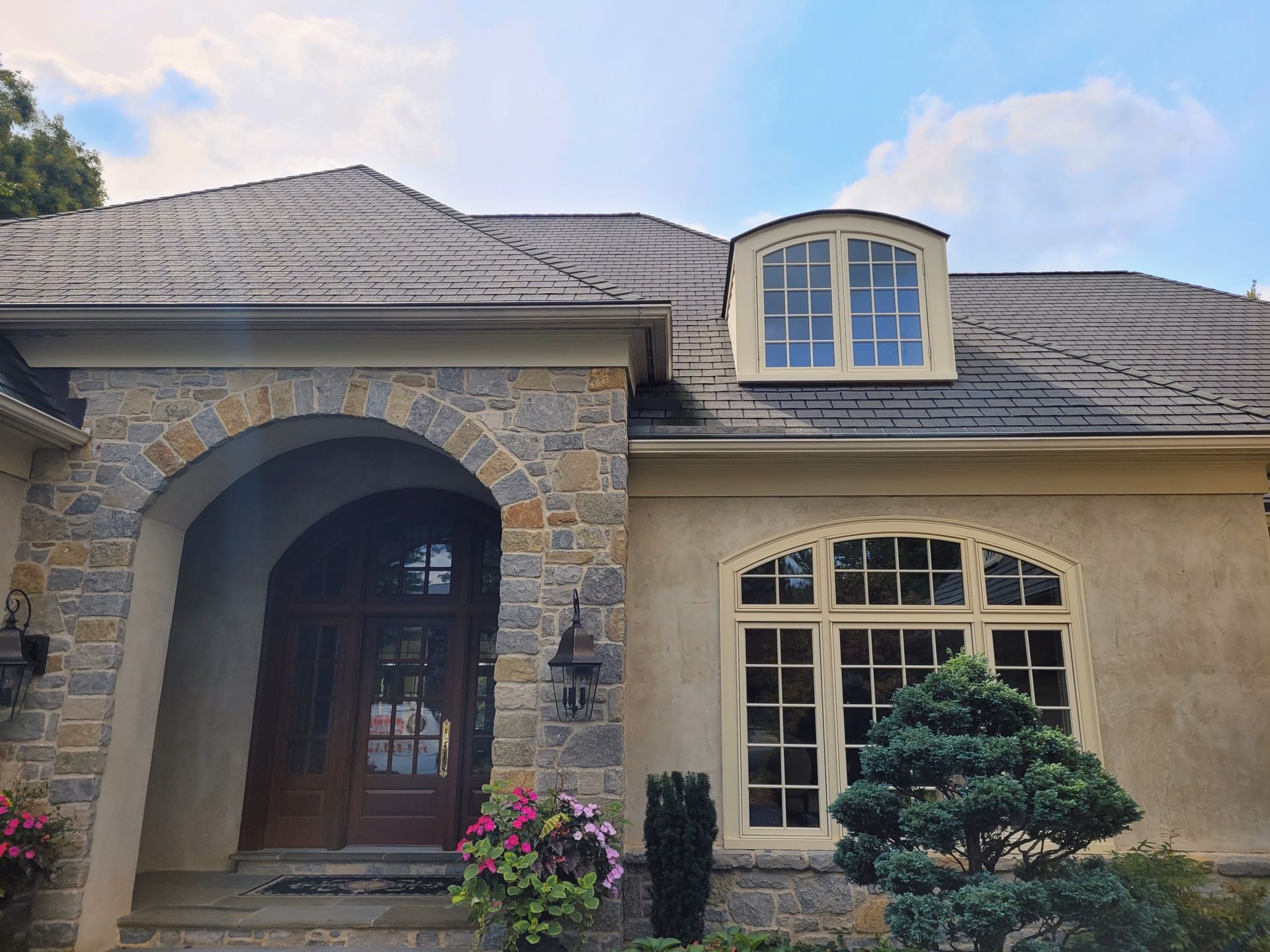 The front of a large house with a slate roof and arched entrance.