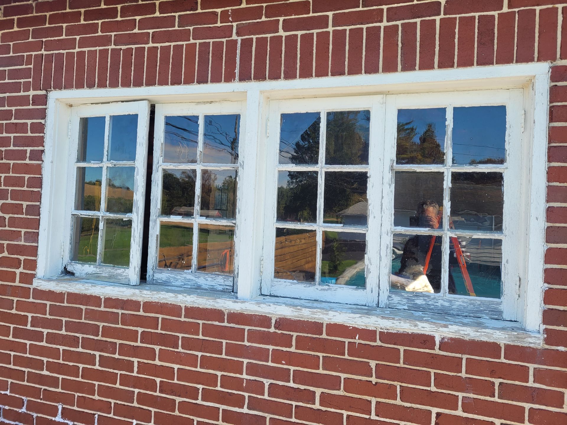 A man is standing in front of a window on a brick building.