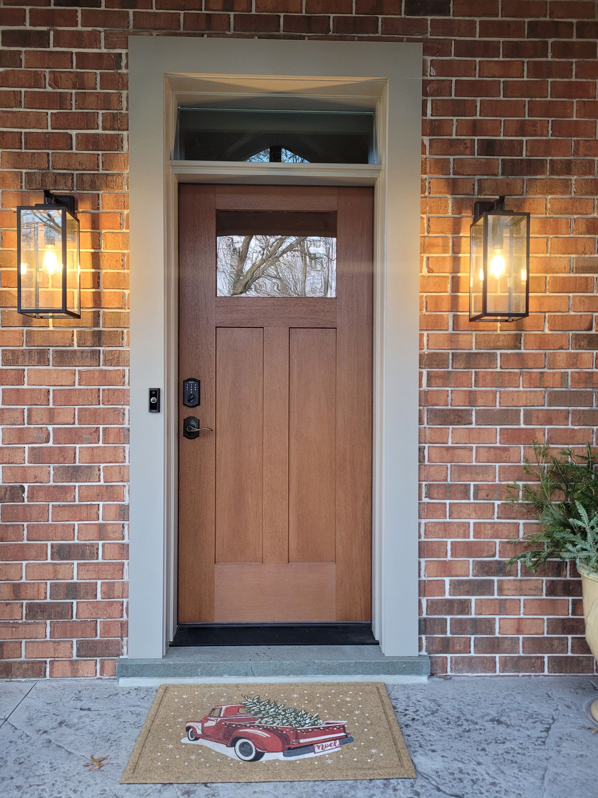 The front door of a brick house with a wooden door and a welcome mat.