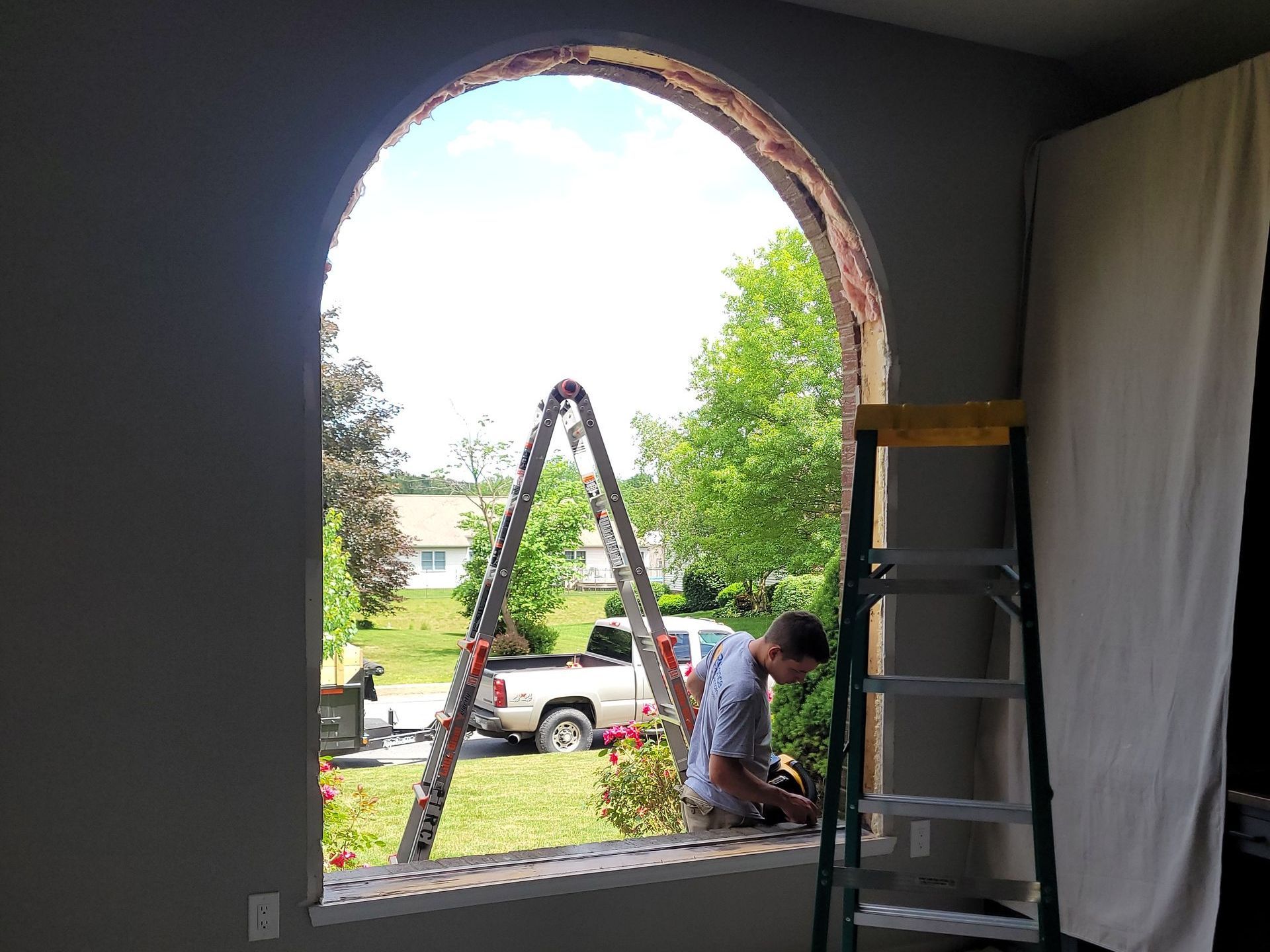A man is working on a window with a ladder in front of it.