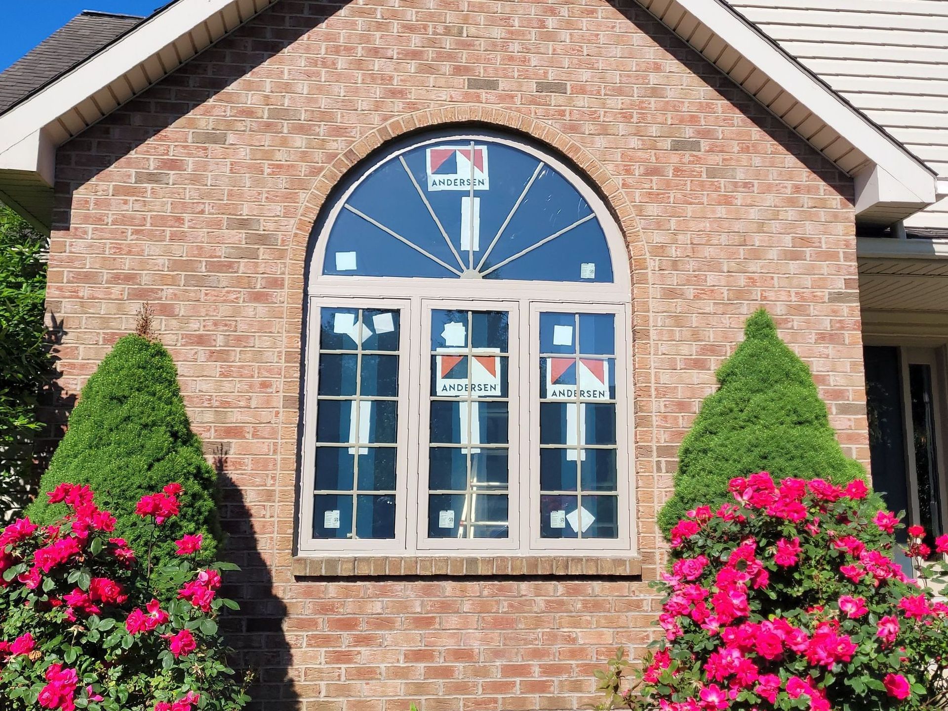 A brick house with a large arched window and pink flowers in front of it.