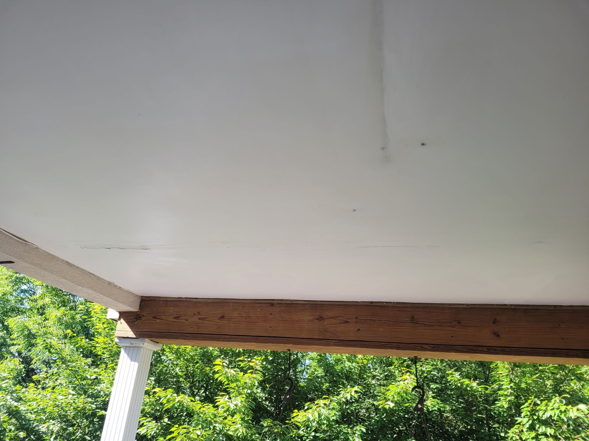 The ceiling of a porch with a wooden beams and trees in the background.
