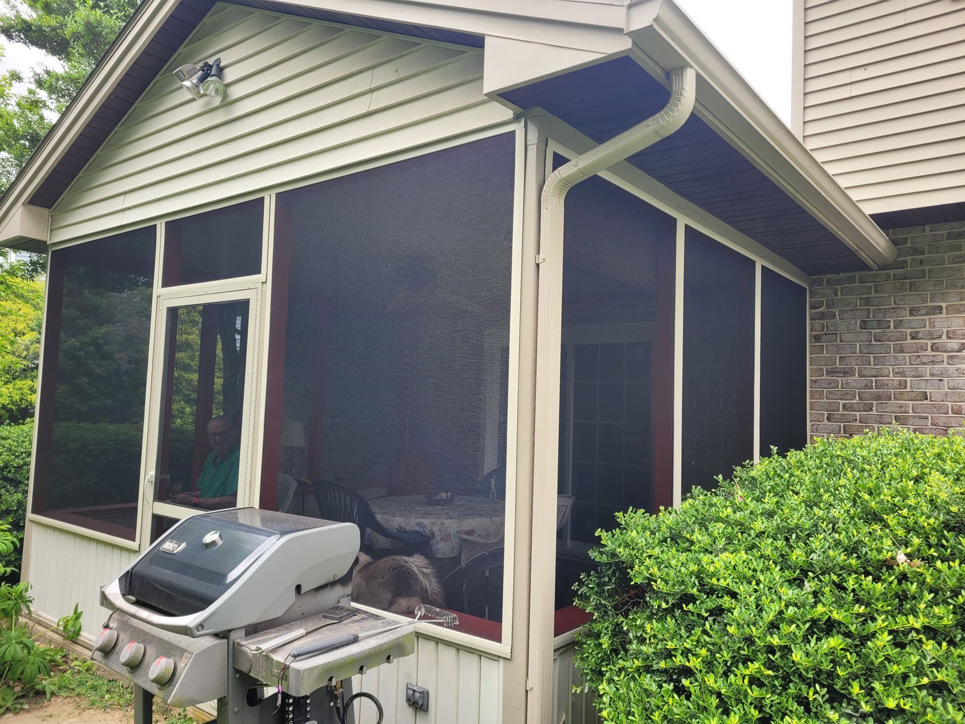 A screened in porch with a grill in front of it.