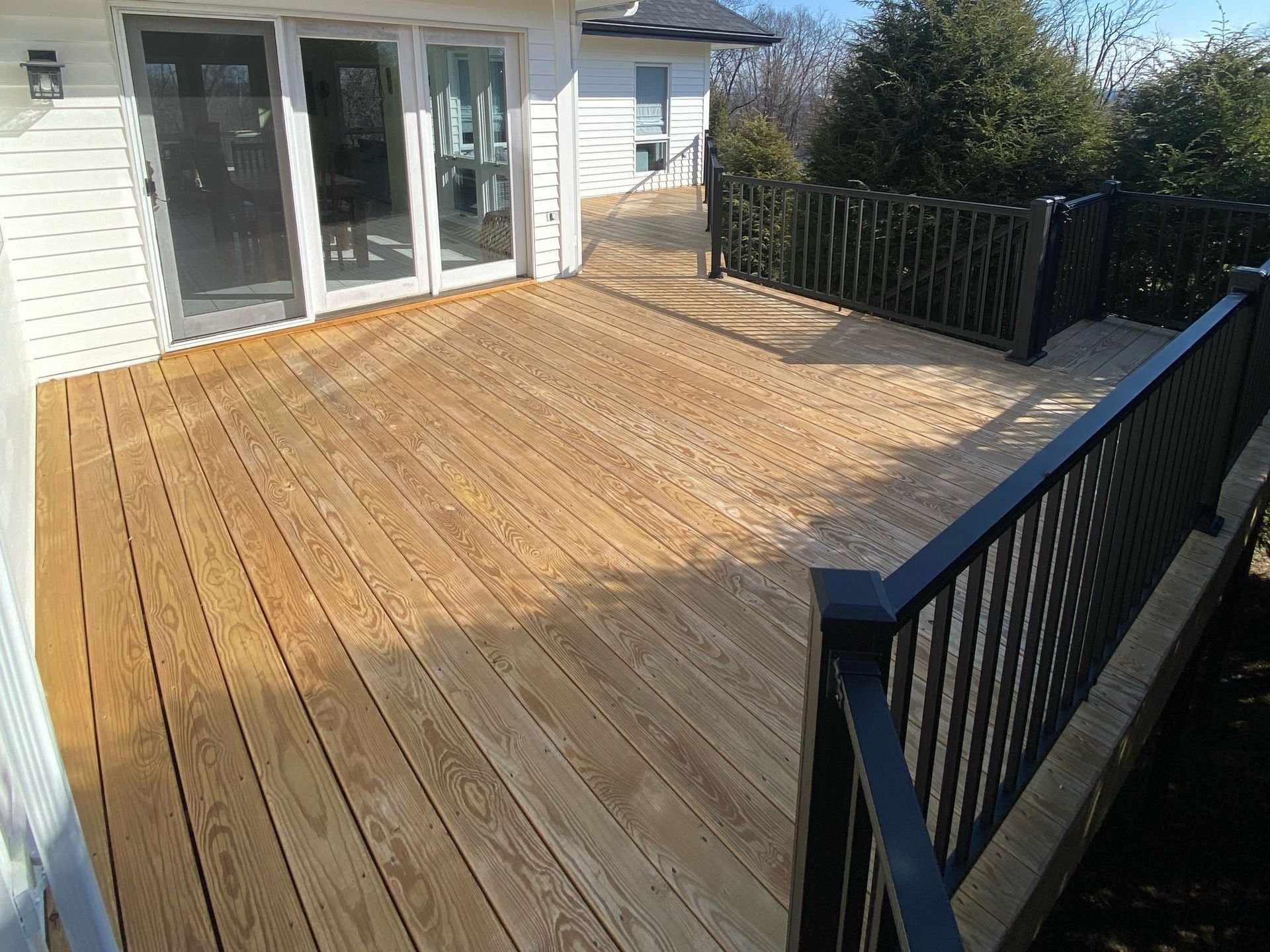 A wooden deck with a black railing and sliding glass doors
