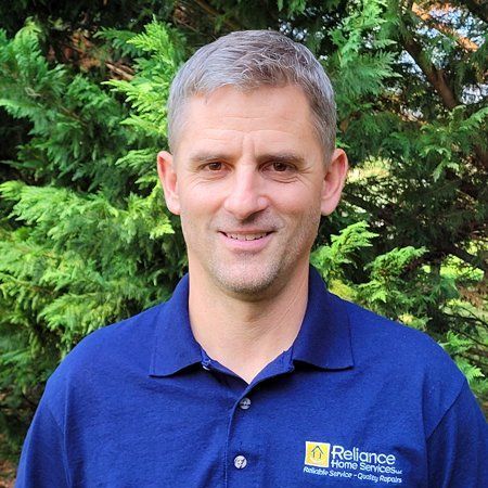 A man in a blue shirt is standing in front of trees.
